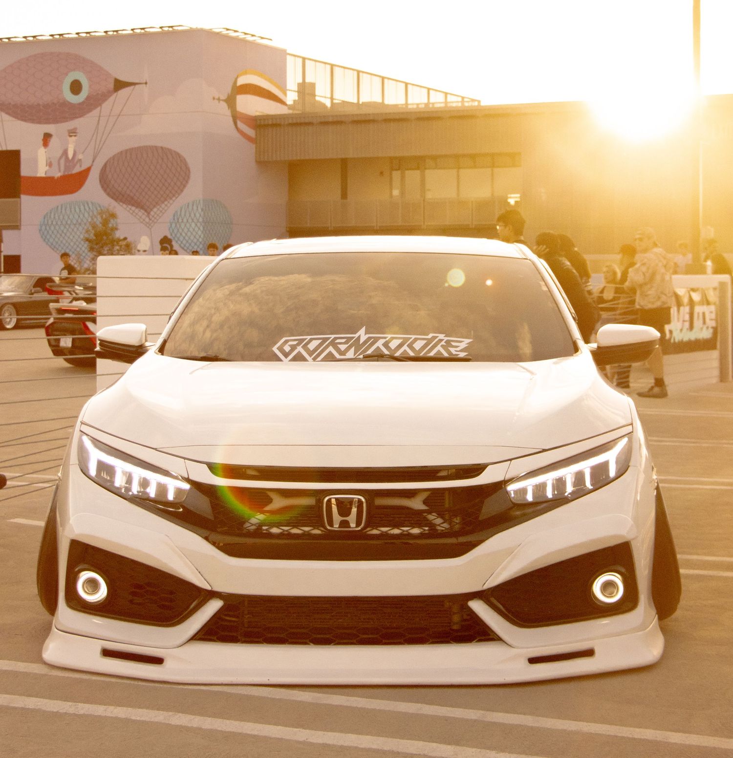 White Honda Civic with custom body kit and LED headlights parked at sunset with golden hour lighting.
