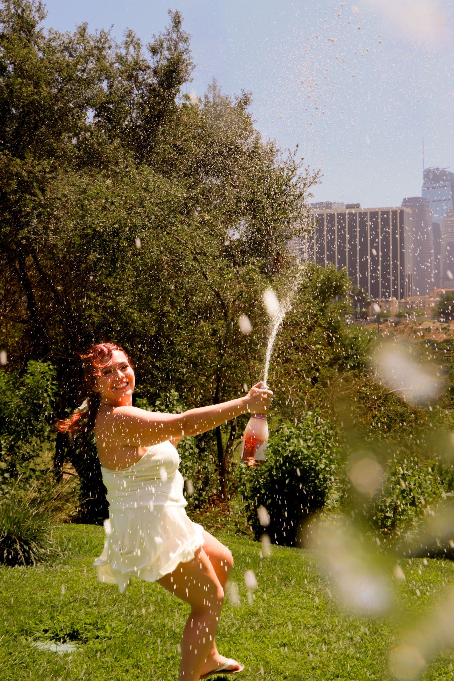 Person in white dress playing with water in a sunny garden.