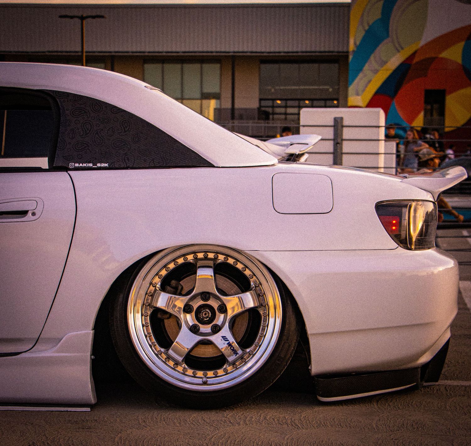 White lowered car with gold and chrome deep dish wheels at a car show, featuring a aggressive stance and custom body kit.