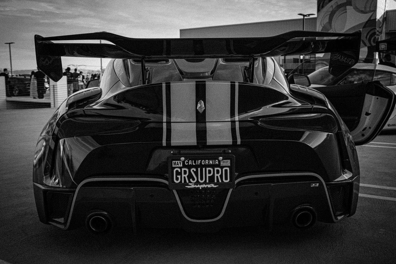 Black and white photo of a Supra sports car with California GRSUPRO license plate and large rear spoiler.