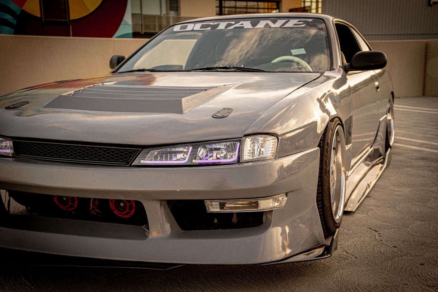Modified silver Nissan S14 with wide body kit, lowered stance, and custom front bumper parked outdoors.