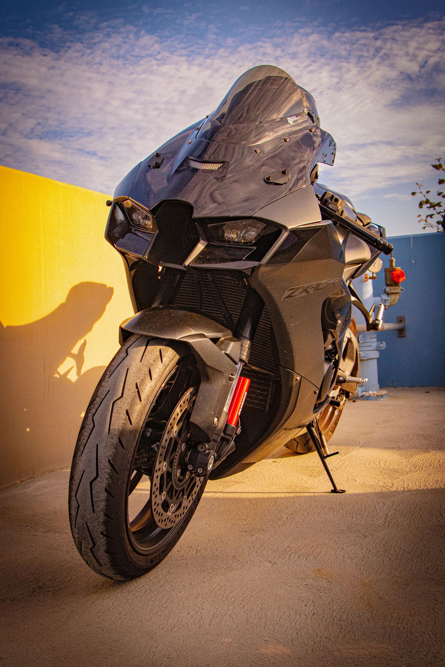 Kawasaki ZX-R sport motorcycle parked against a yellow wall under a blue sky with dramatic golden hour lighting.