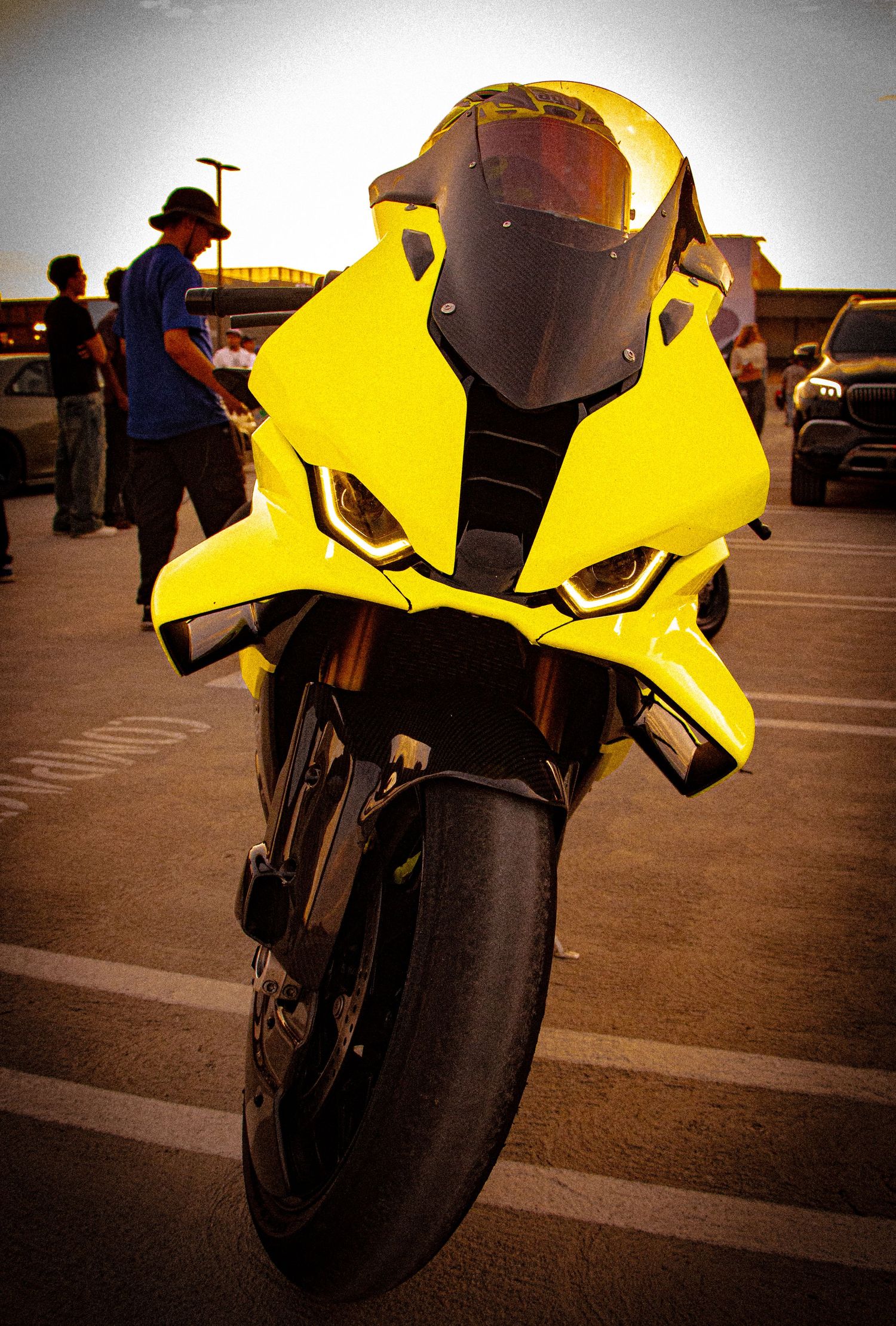 Bright yellow sport motorcycle parked in a lot, featuring aggressive styling, dark windscreen, and LED headlights at dusk.