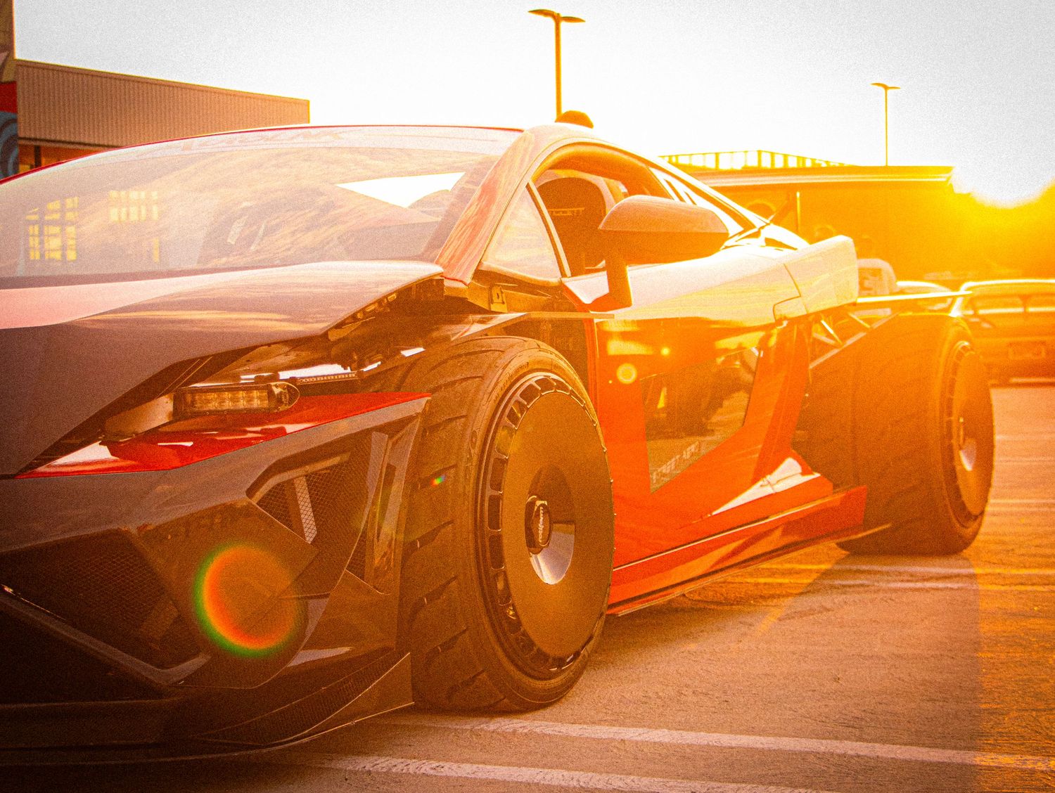 Sleek black supercar parked at sunset with golden light reflecting off its aerodynamic body and wide racing tires.