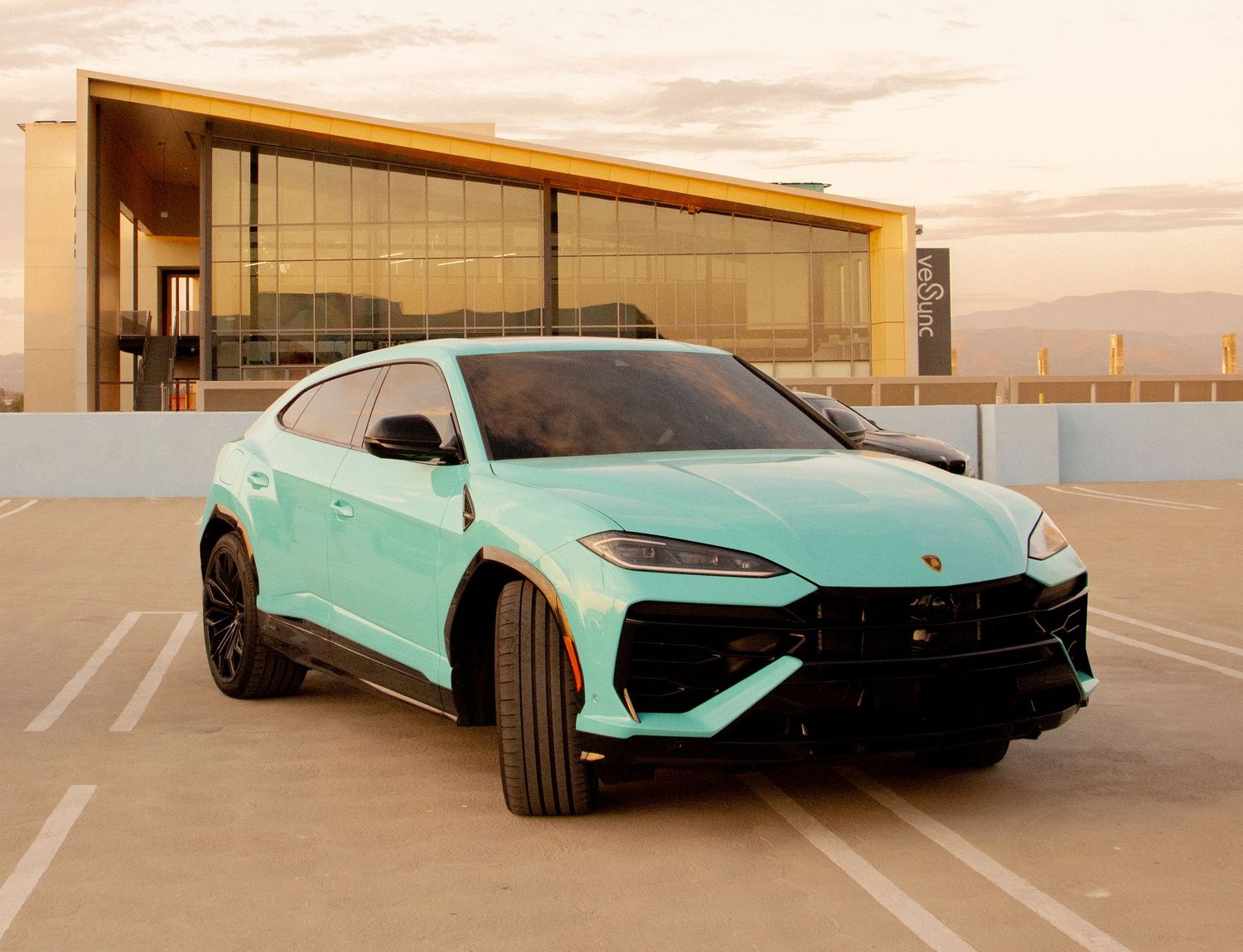 Mint green Lamborghini Urus SUV parked on rooftop lot at sunset with modern building backdrop.