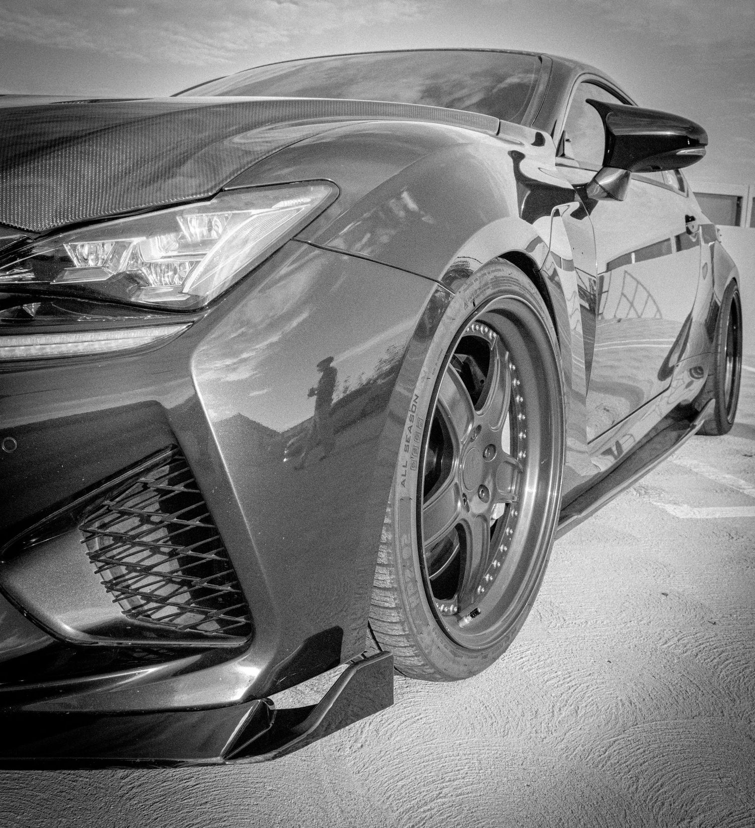 Black and white photo of a sleek modified Lexus sports car with custom alloy wheels and aggressive front bumper styling.
