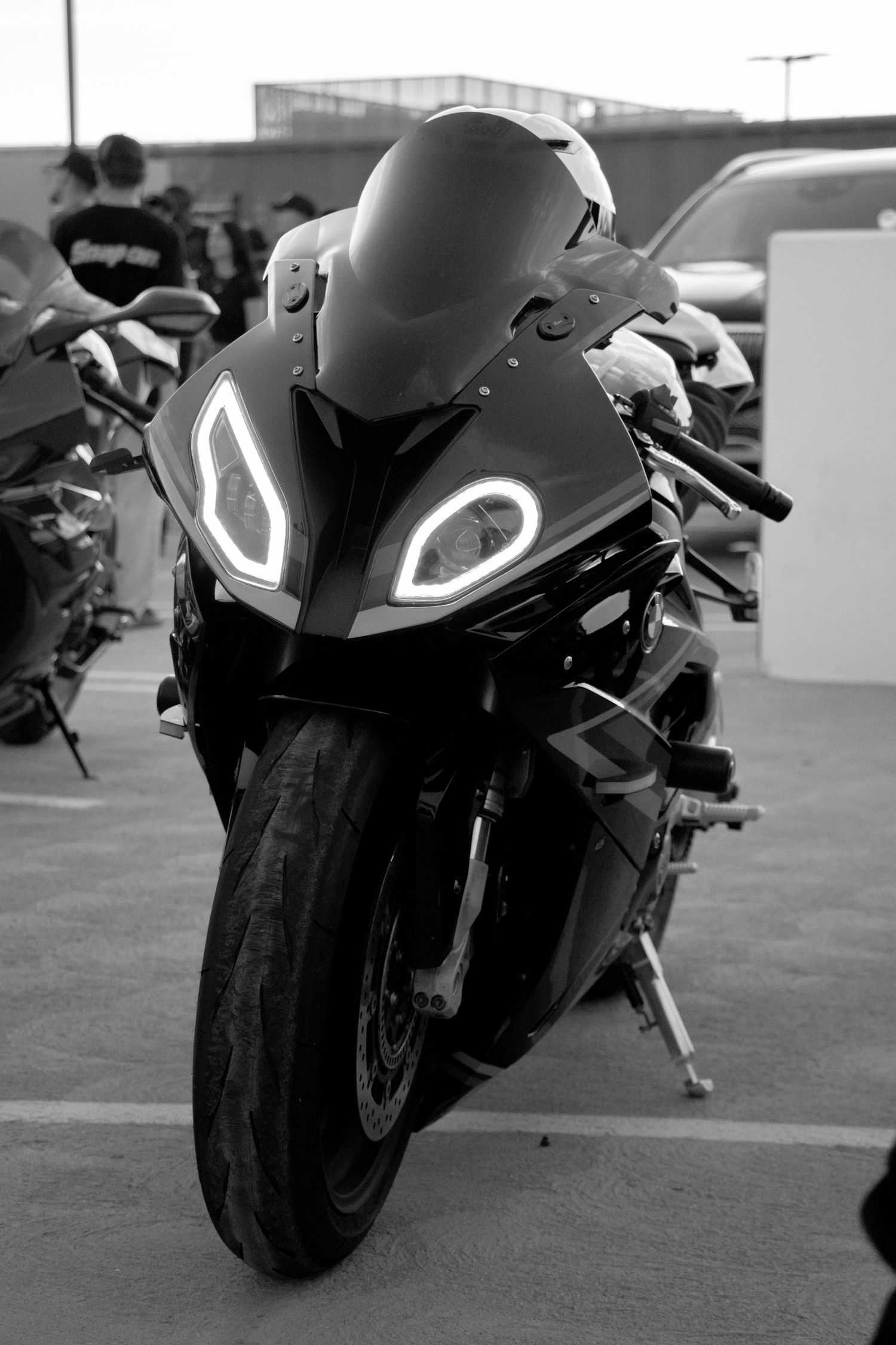 Black and white photo of a sport motorcycle with LED headlights parked in a lot, front view close-up.