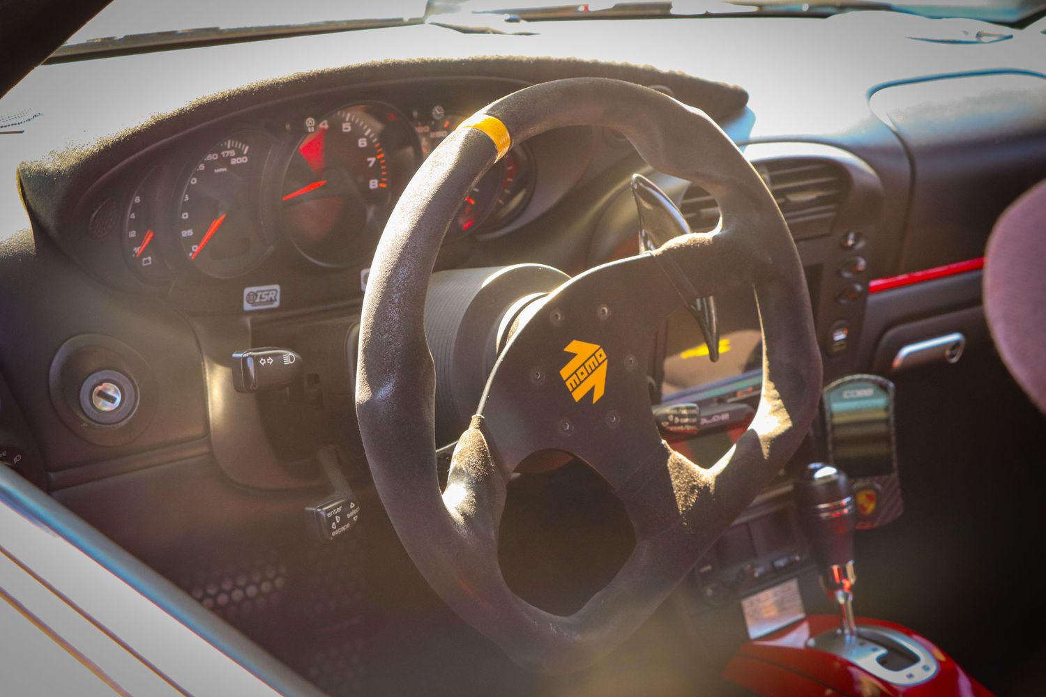 Sports car interior dashboard with racing steering wheel illuminated by sunlight.