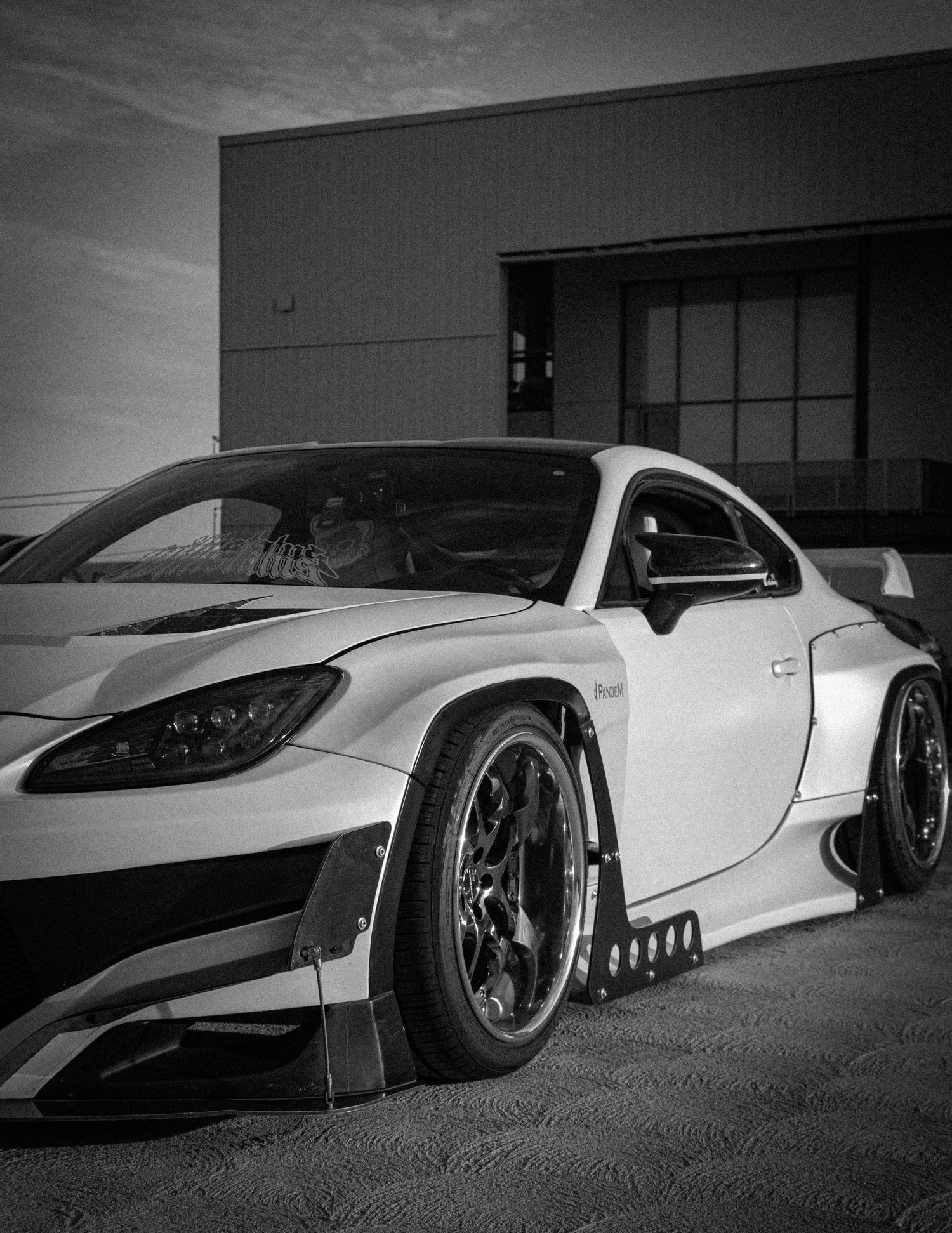 Black and white photo of a heavily modified widebody sports car with aggressive aero kit parked outside a building.