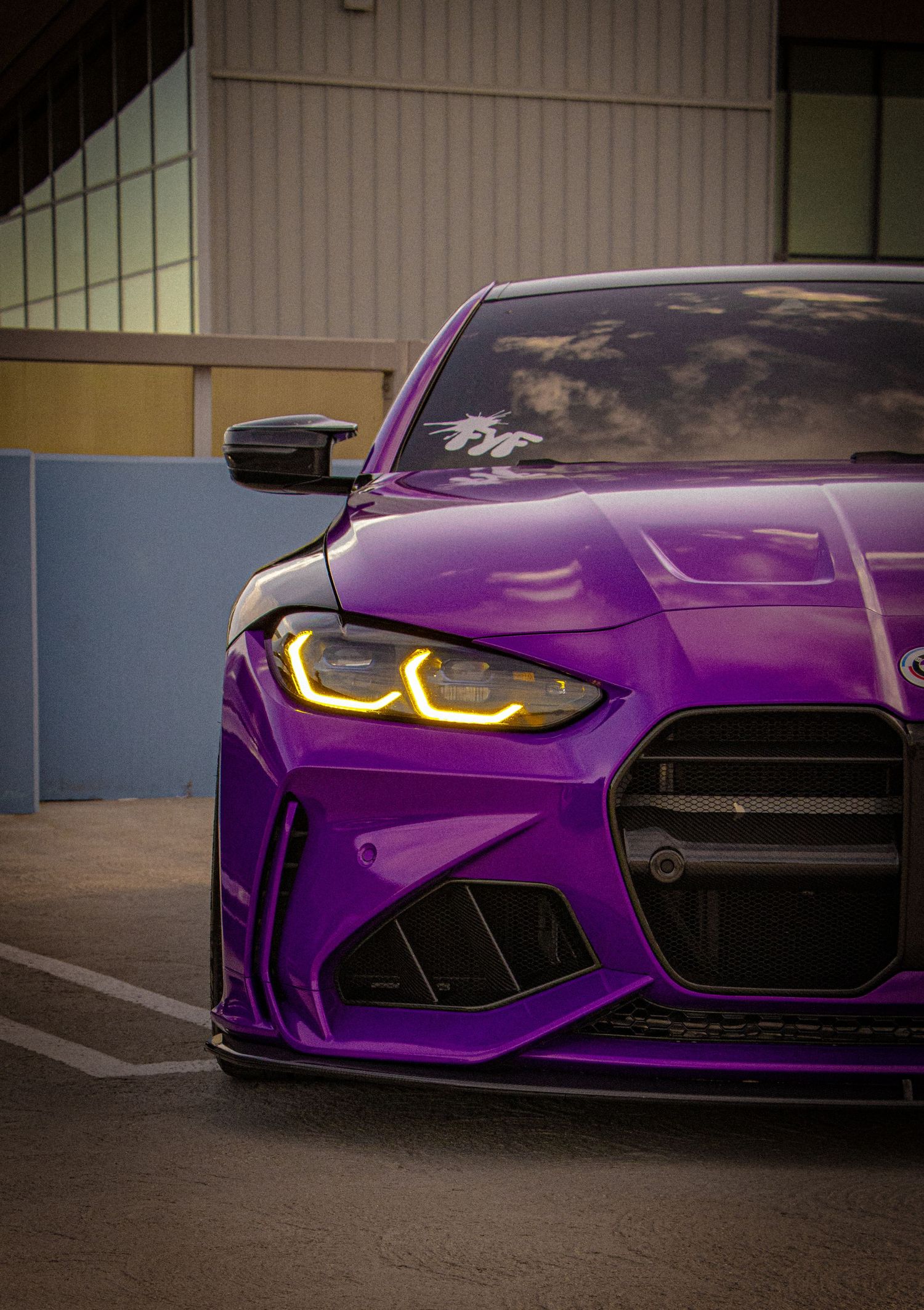 Purple BMW M4 with yellow LED headlights and large kidney grille, custom widebody kit, parked near a building.