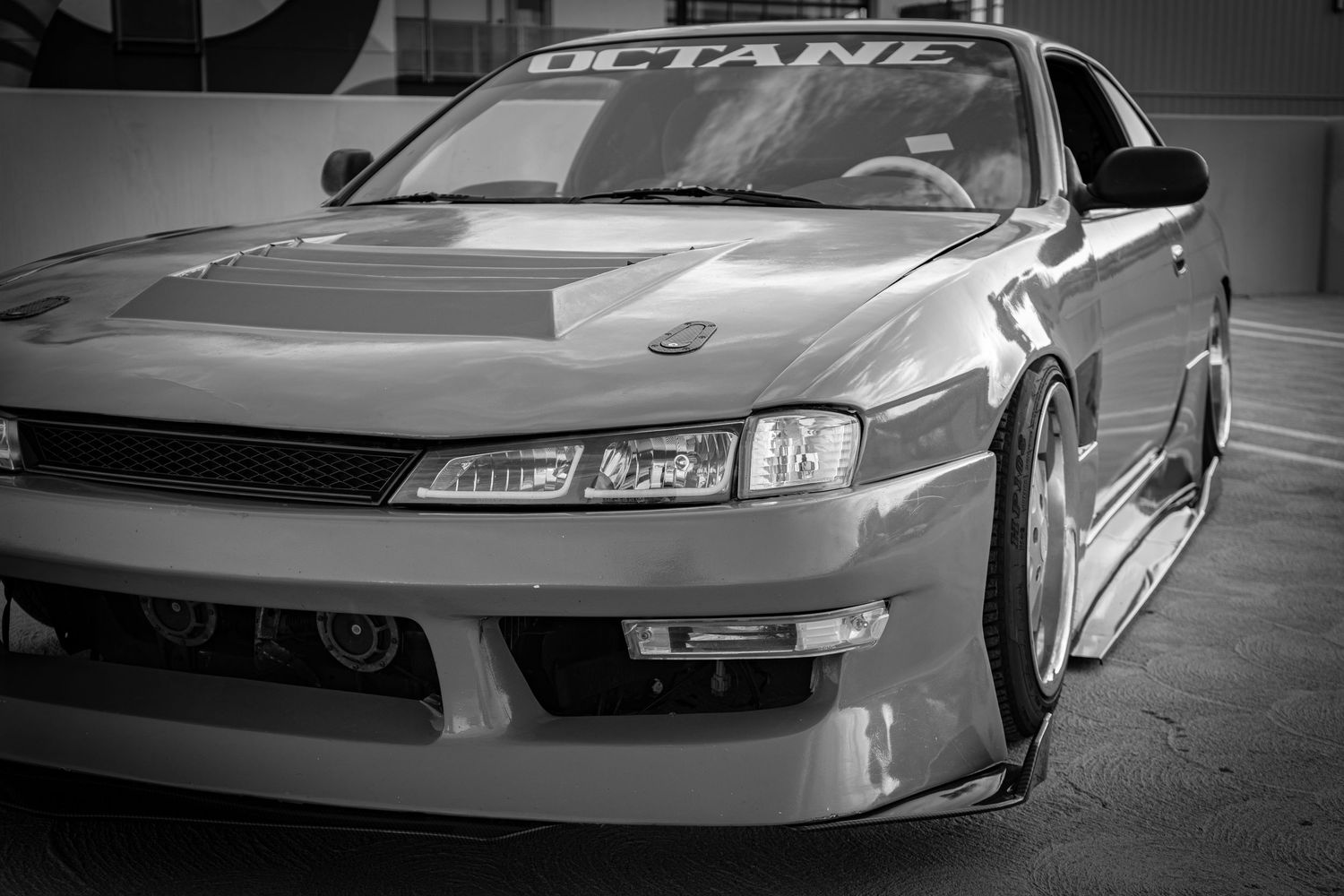 Black and white photo of a modified Nissan S14 sports car with custom body kit and Octane branding on windshield.