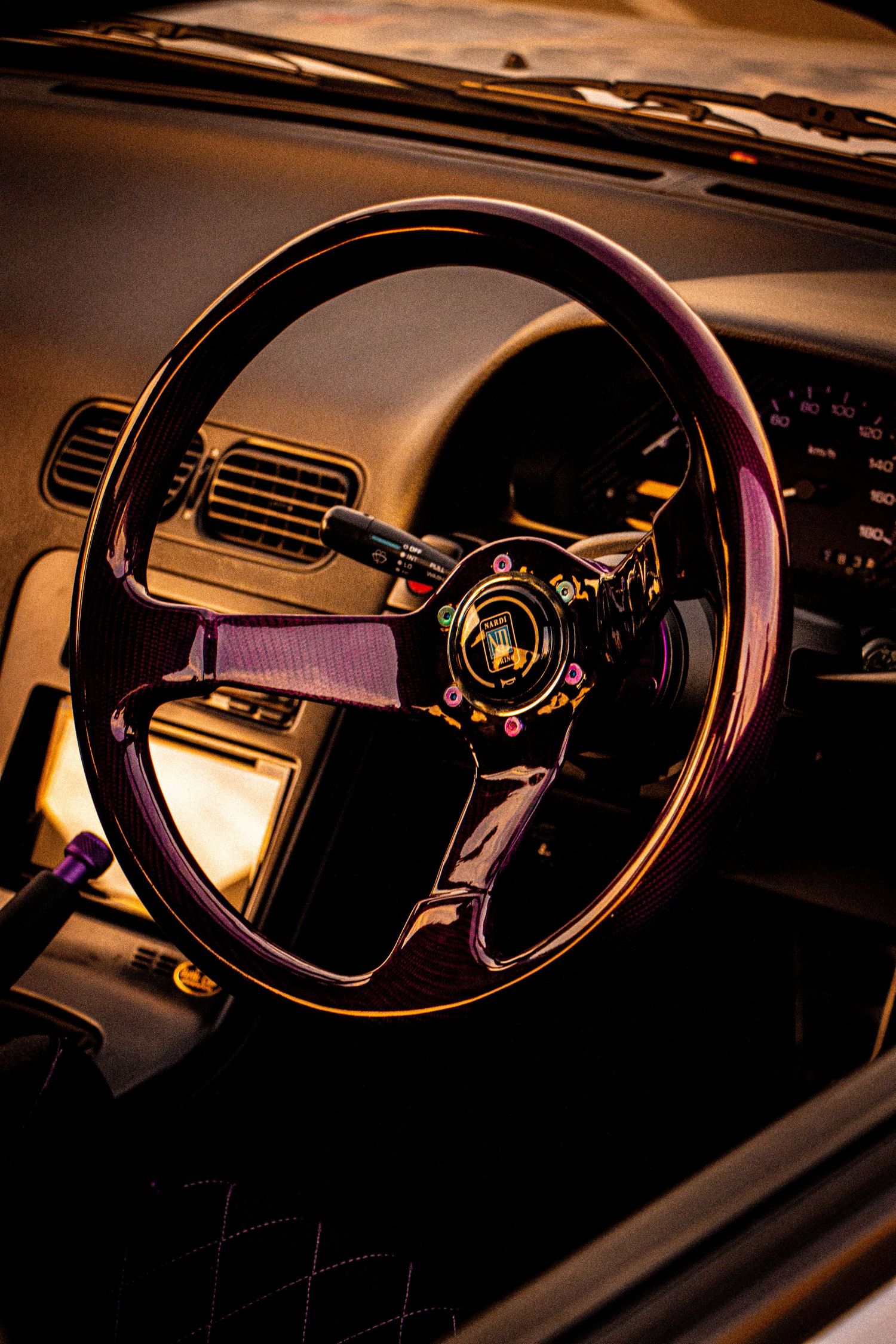 Custom aftermarket steering wheel with gold center hub and purple accents inside a vintage car interior.