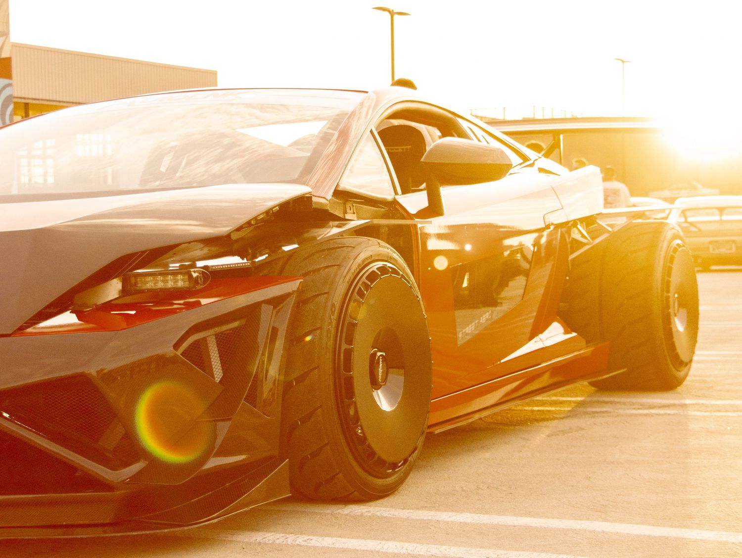 A sleek black sports race car parked in a lot, bathed in golden sunset light with dramatic low-angle perspective.