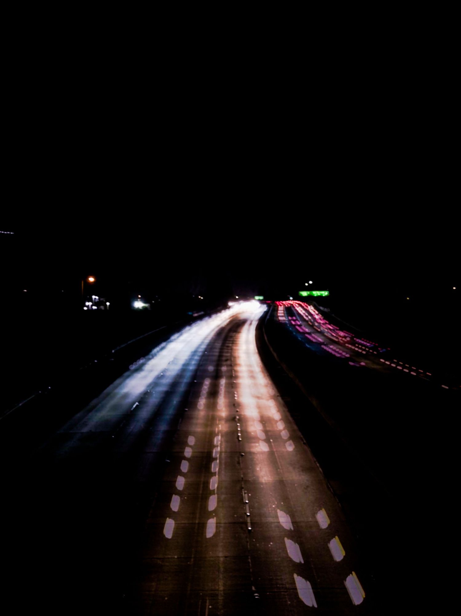 Long exposure shot of highway traffic lights creating light trails at night.