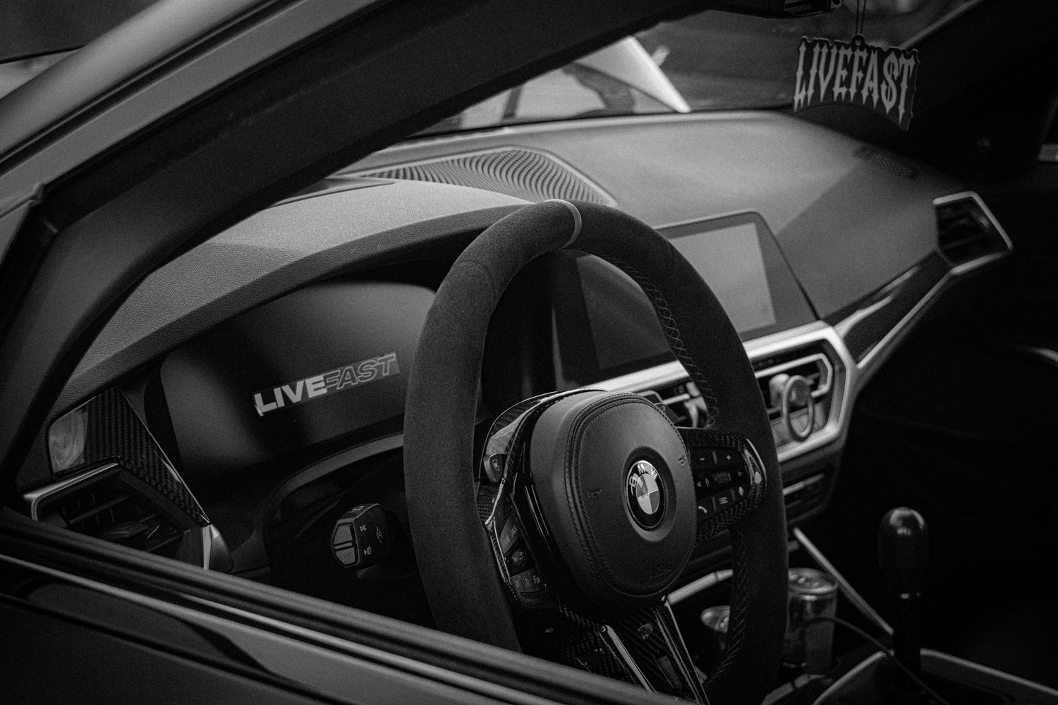 Black and white BMW interior showcasing steering wheel and dashboard with LiveFast branding in a luxury sports car.