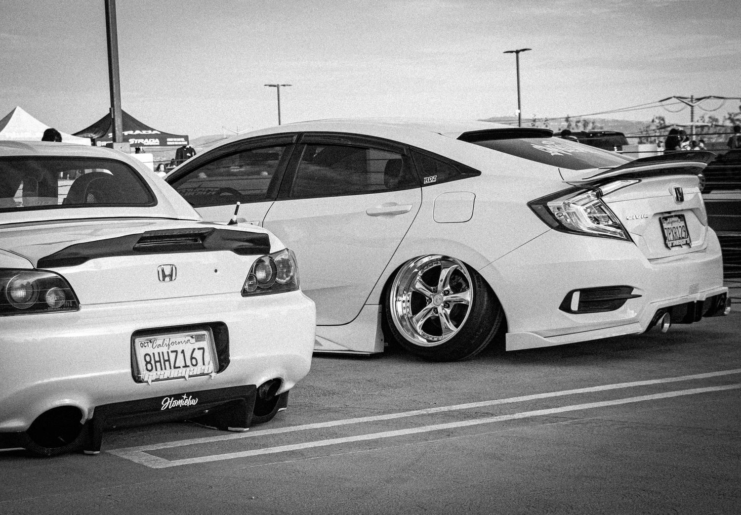 Two modified Honda cars, including a lowered white Honda Civic with wide body kit, parked at a car show.