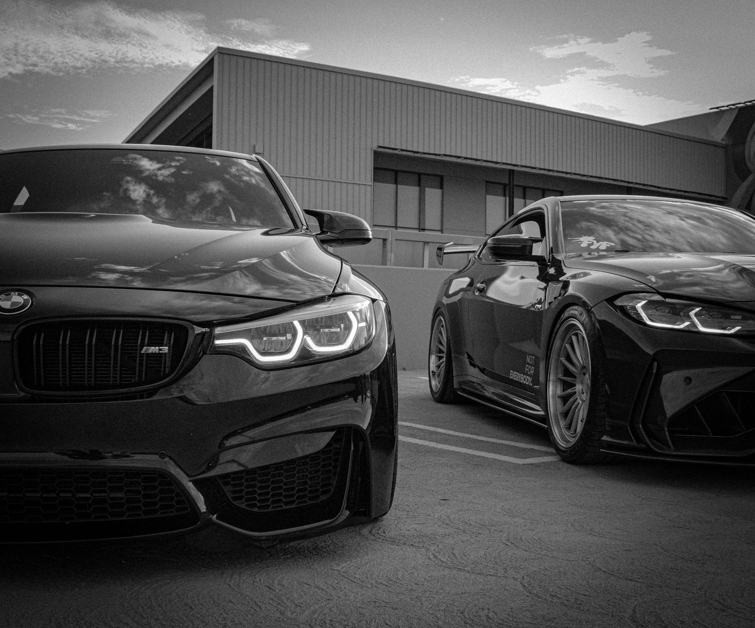 Two sleek black BMW M4 sports cars parked side by side in a dramatic black and white automotive photo.
