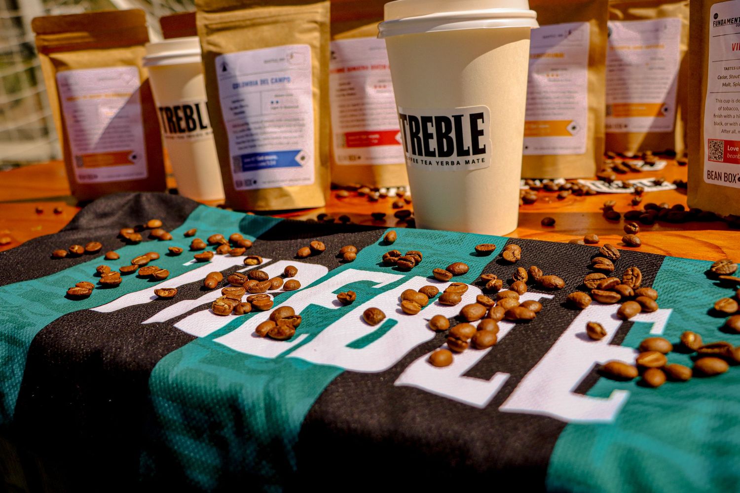 Coffee beans scattered on piano keys with disposable coffee cups on turquoise fabric.