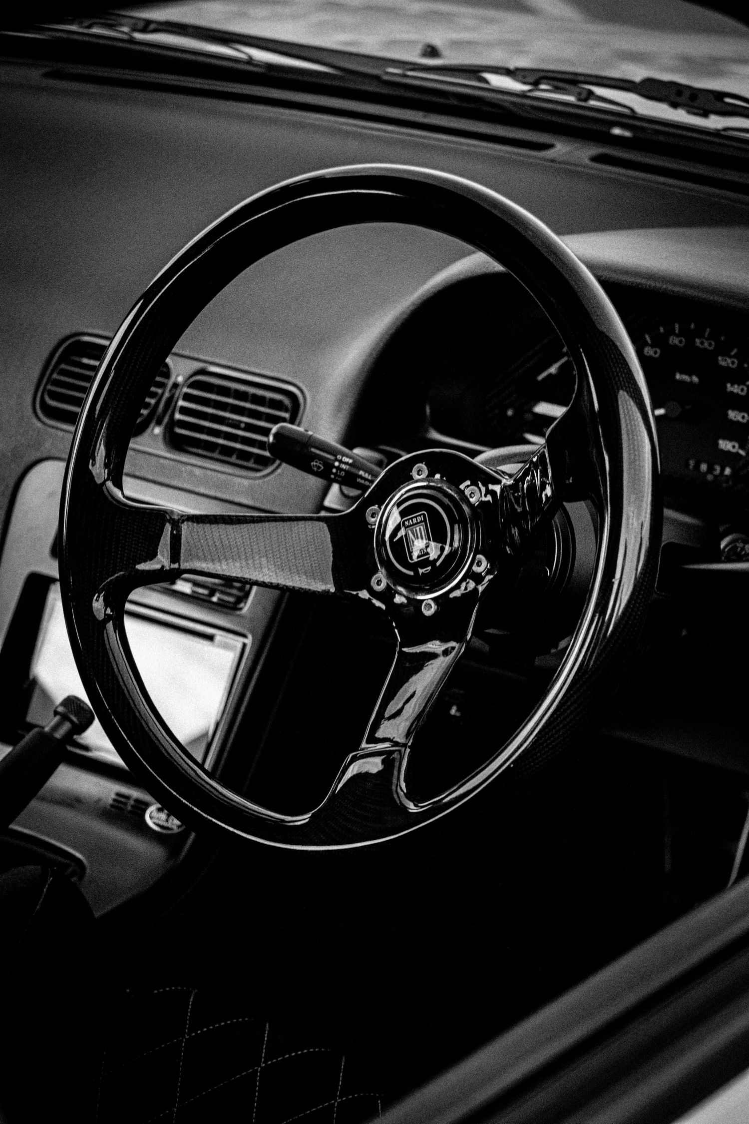Black and white photo of a sporty aftermarket steering wheel inside a classic car interior.