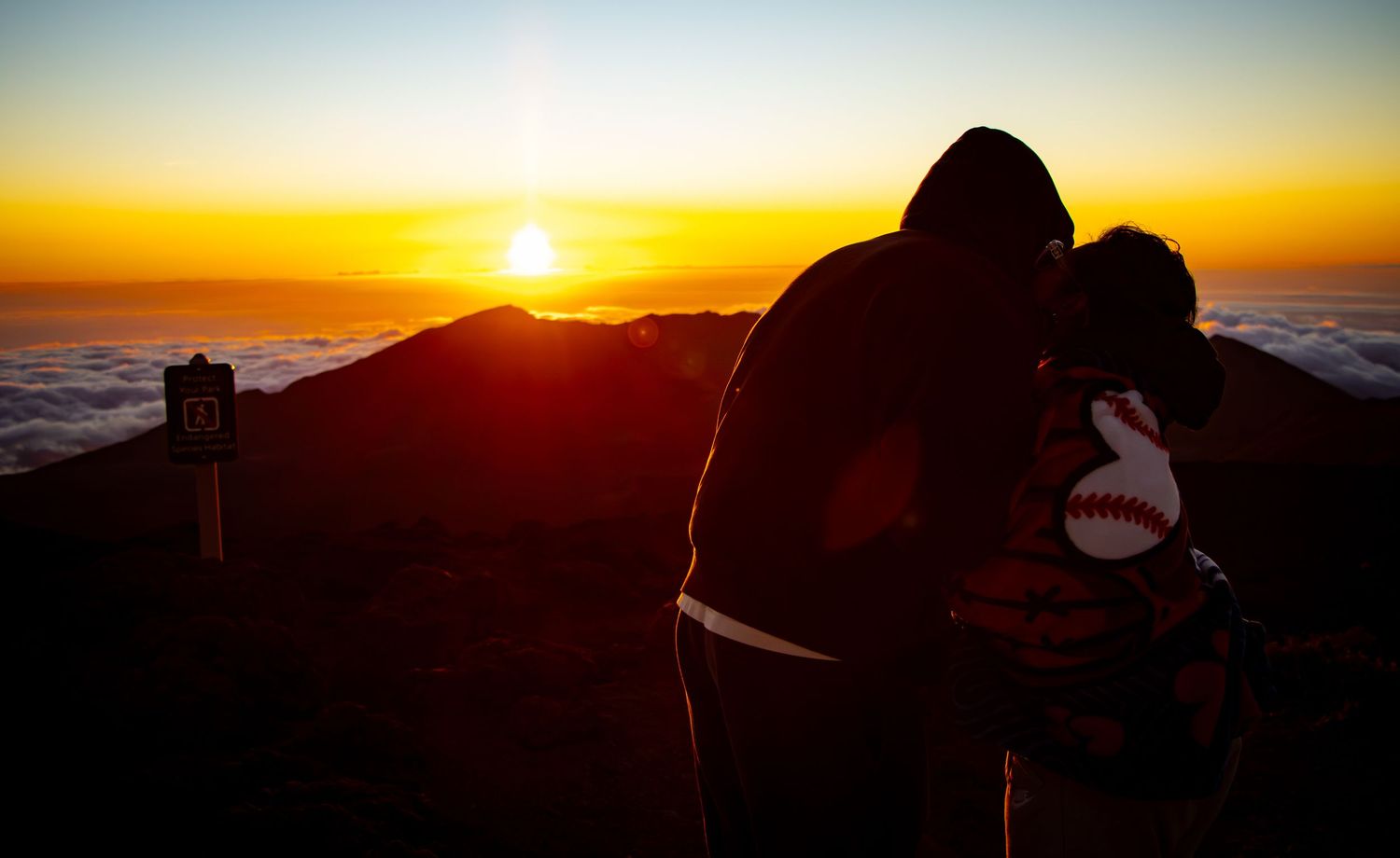 Silhouettes watching sunset from mountain summit.