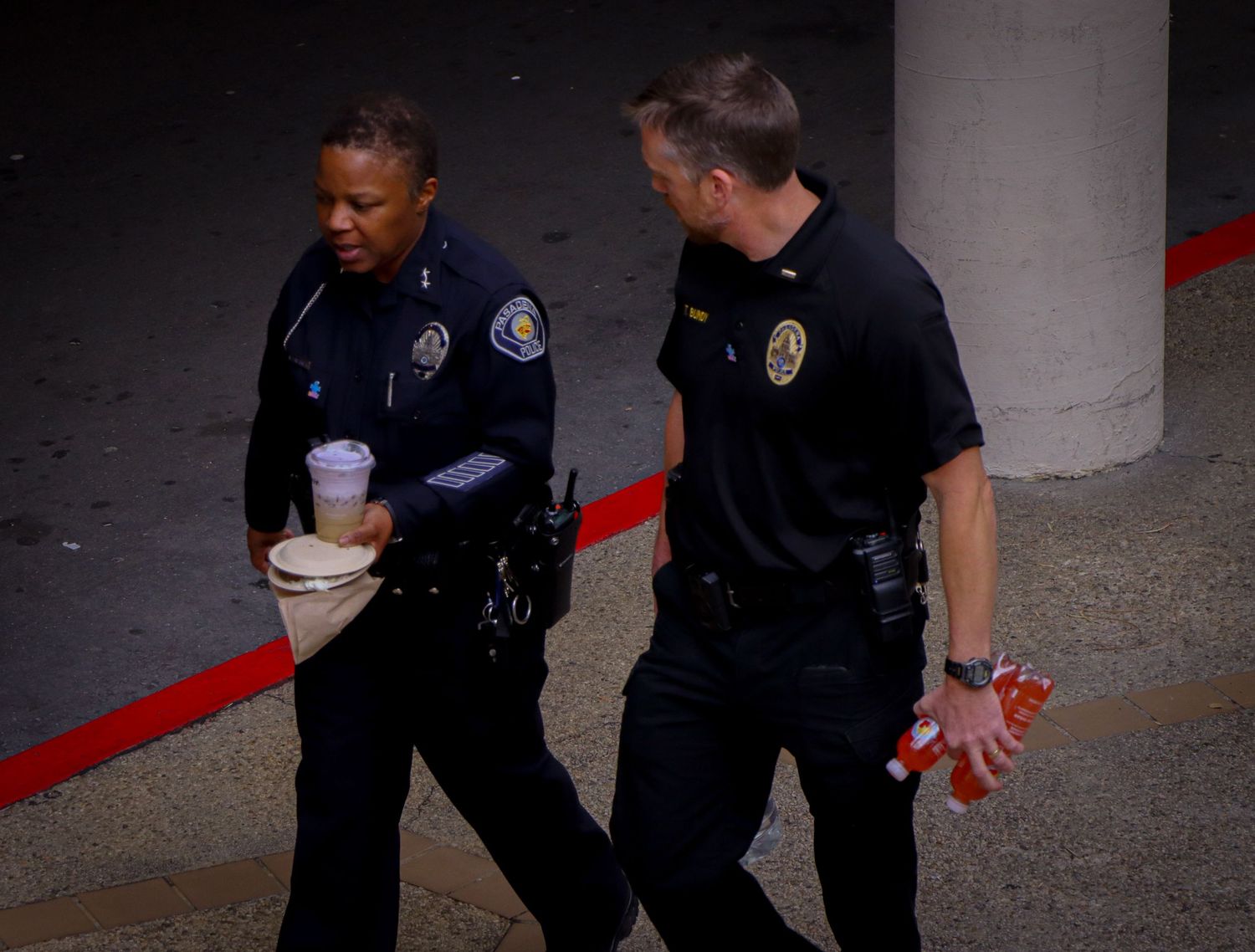Two police officers in dark uniforms walking together while holding coffee cups.