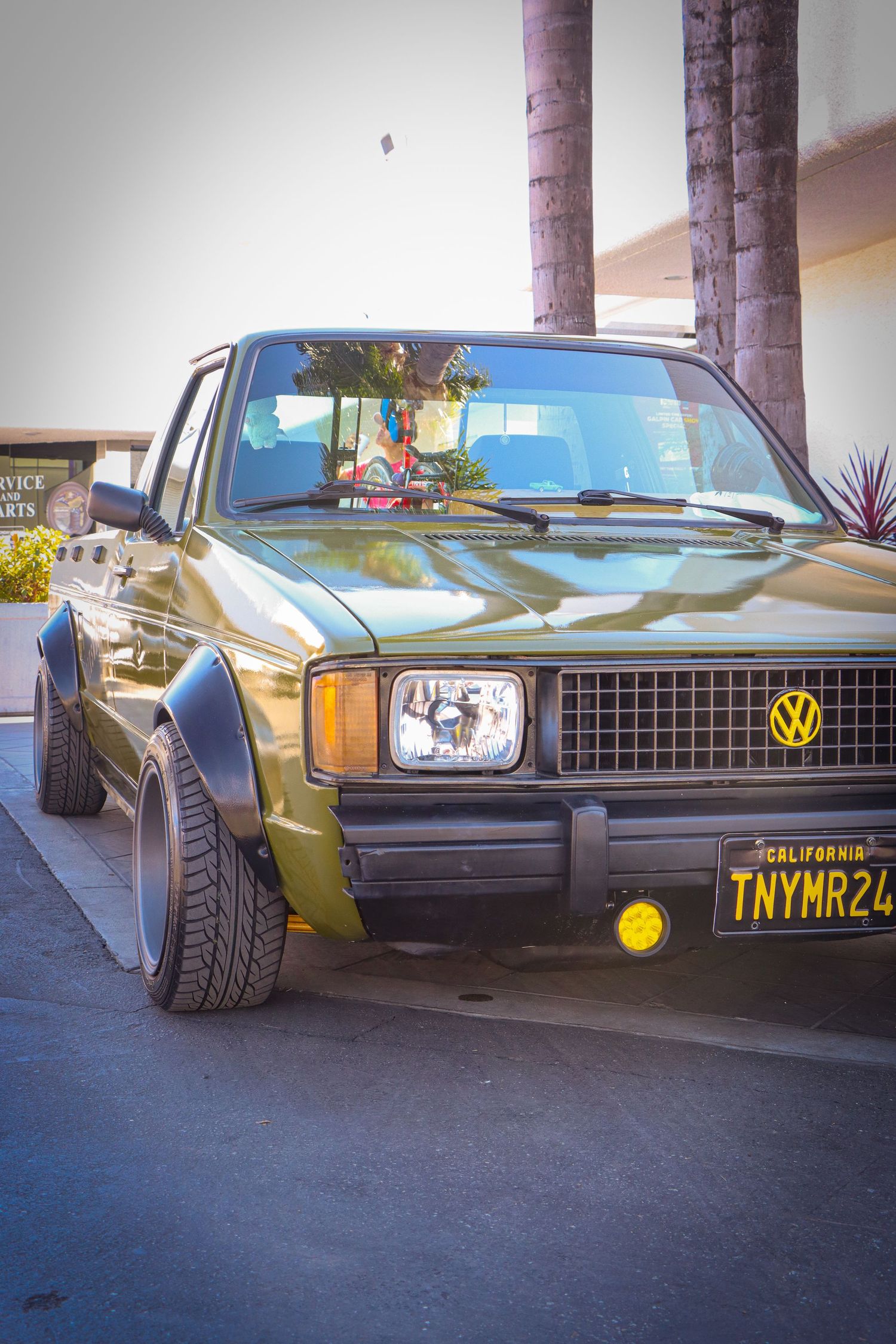 Modified vintage Volkswagen Rabbit in olive green with yellow fog lights.