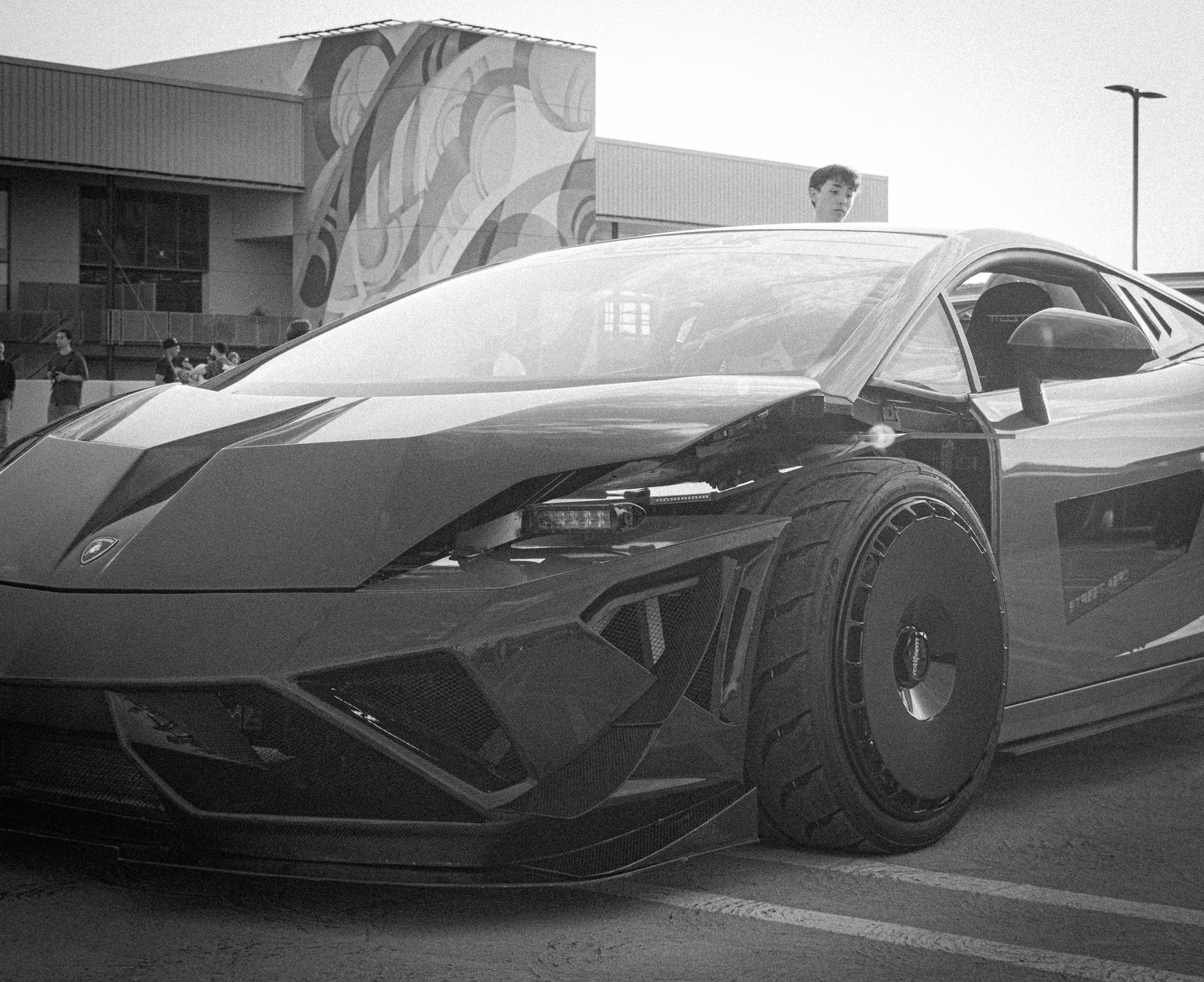 Black and white photo of a modified Lamborghini Gallardo with wide body kit at a car show.
