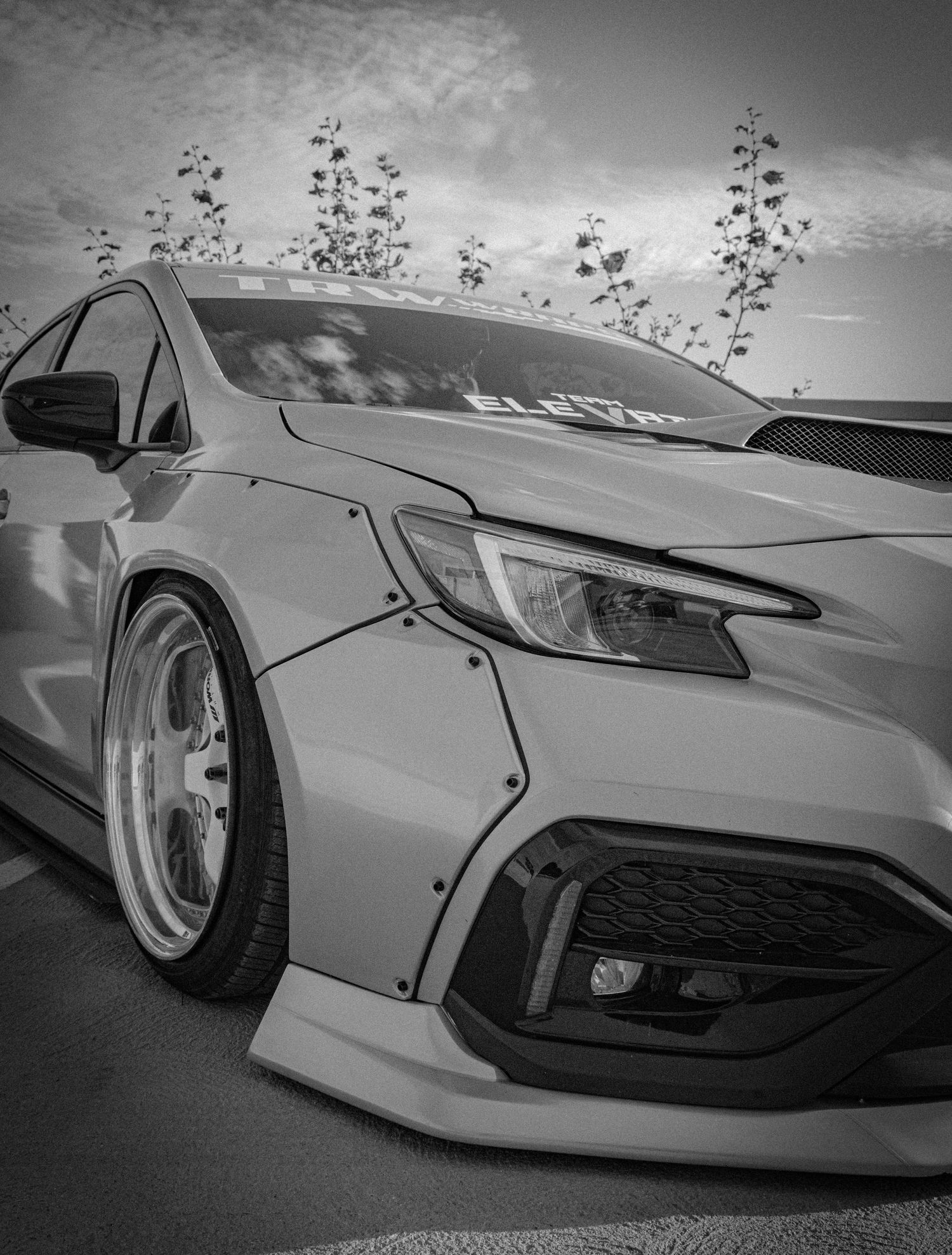Black and white photo of a widebody-kitted Honda Civic with aggressive front bumper and deep-dish wheels at a car show.
