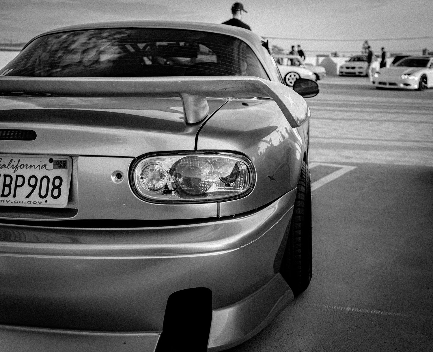 Black and white photo of a California-plated Toyota Supra with wide body kit at a car meet.