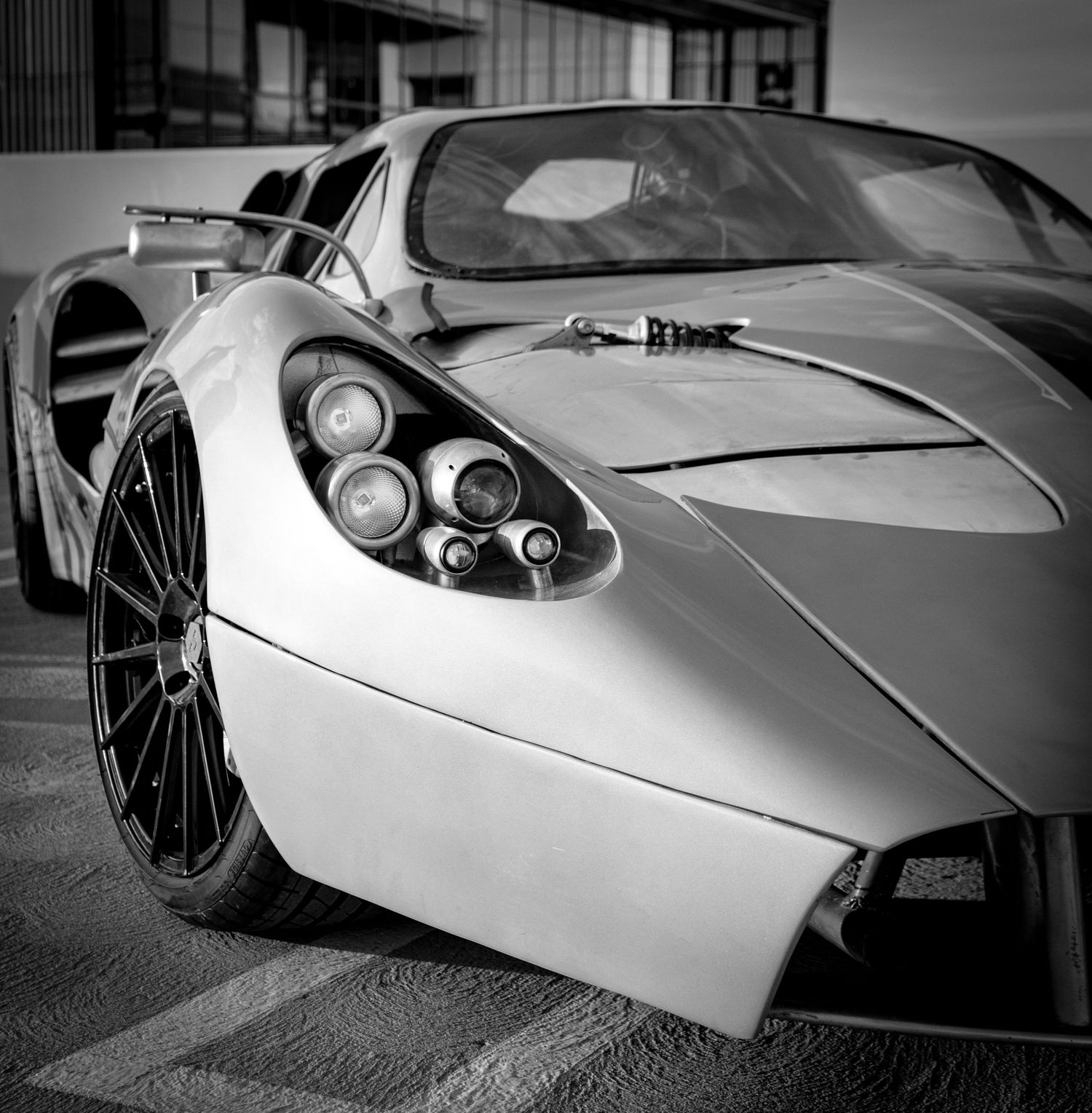 Black and white close-up of a sleek supercar showcasing its distinctive quad headlights and aerodynamic bodywork.