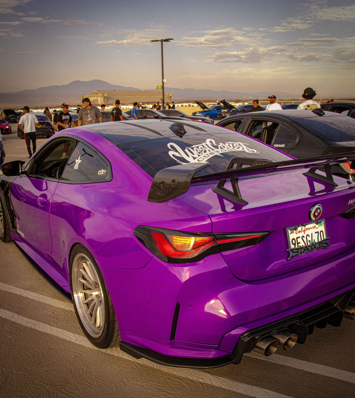 Purple Lexus RC F with large rear spoiler and wide body kit at a car show in a sunny parking lot.