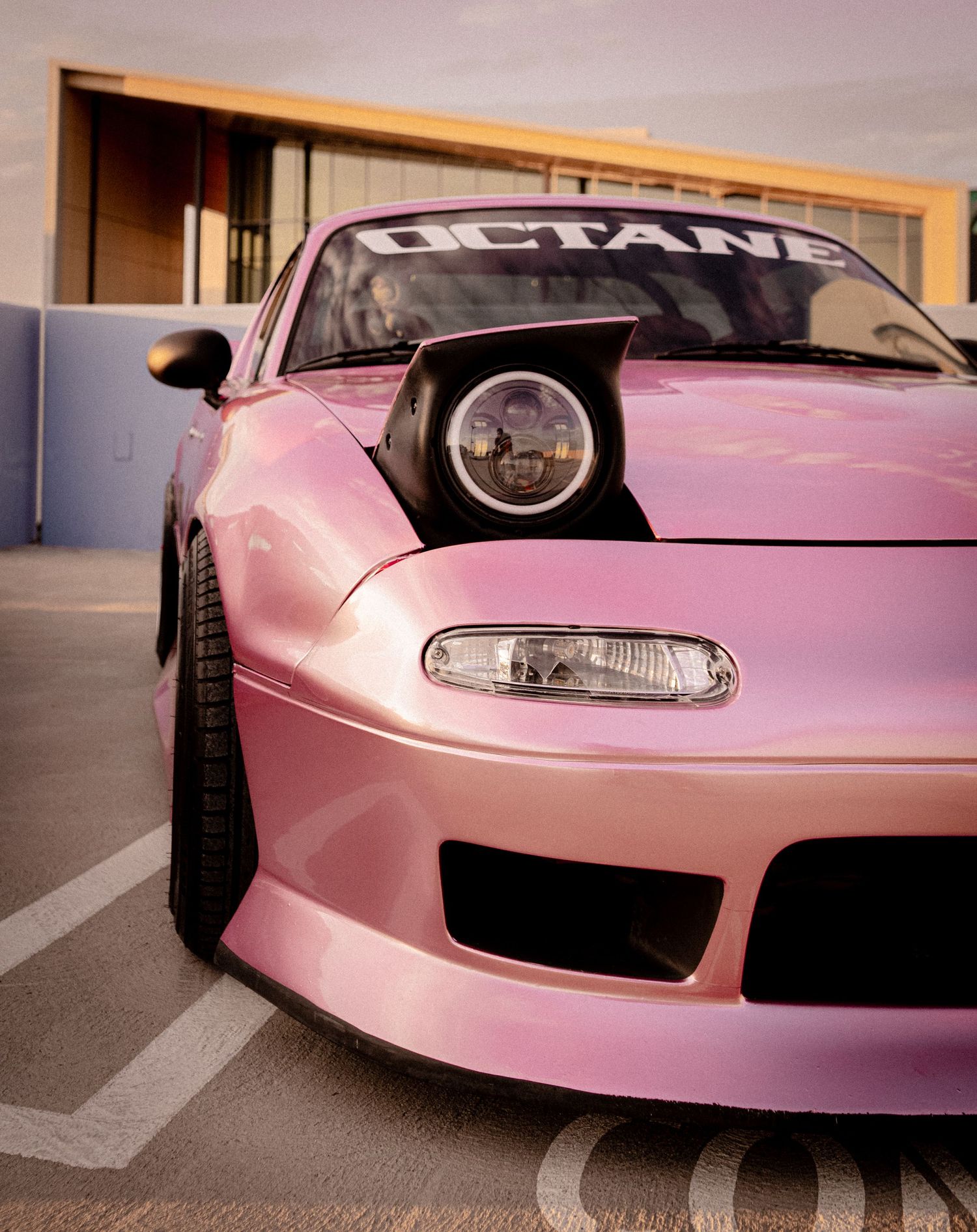 Pink modified sports car with wide body kit and Octane windshield banner parked in a lot, front fascia view.
