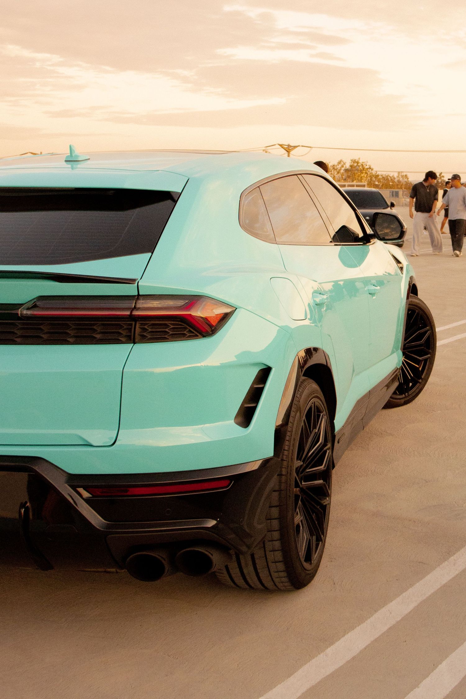 Mint green Lamborghini Urus SUV rear view with black wheels at sunset in a parking lot.