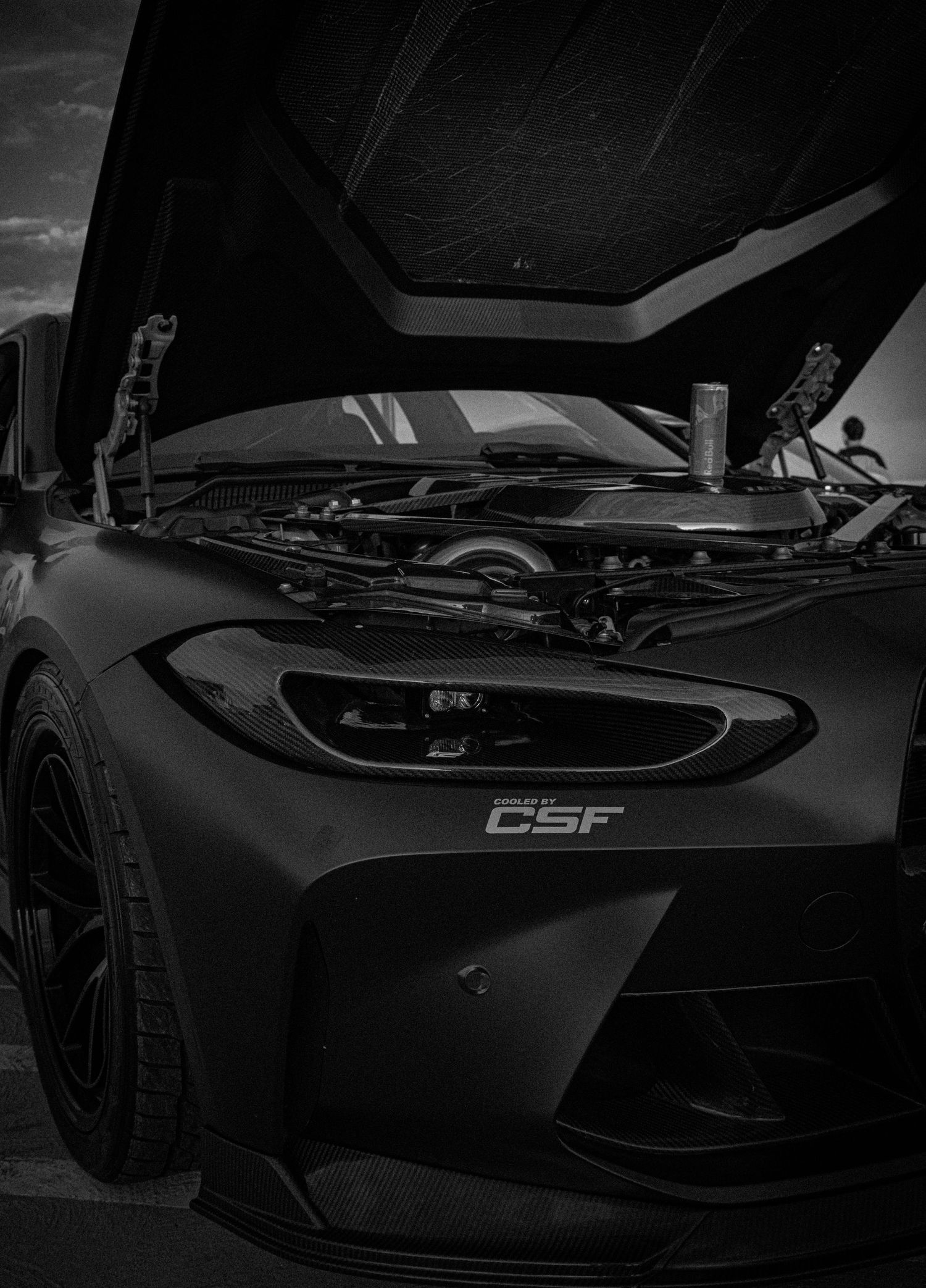 Black sports car with hood open revealing engine bay, featuring CSF branding on front bumper in dramatic monochrome.