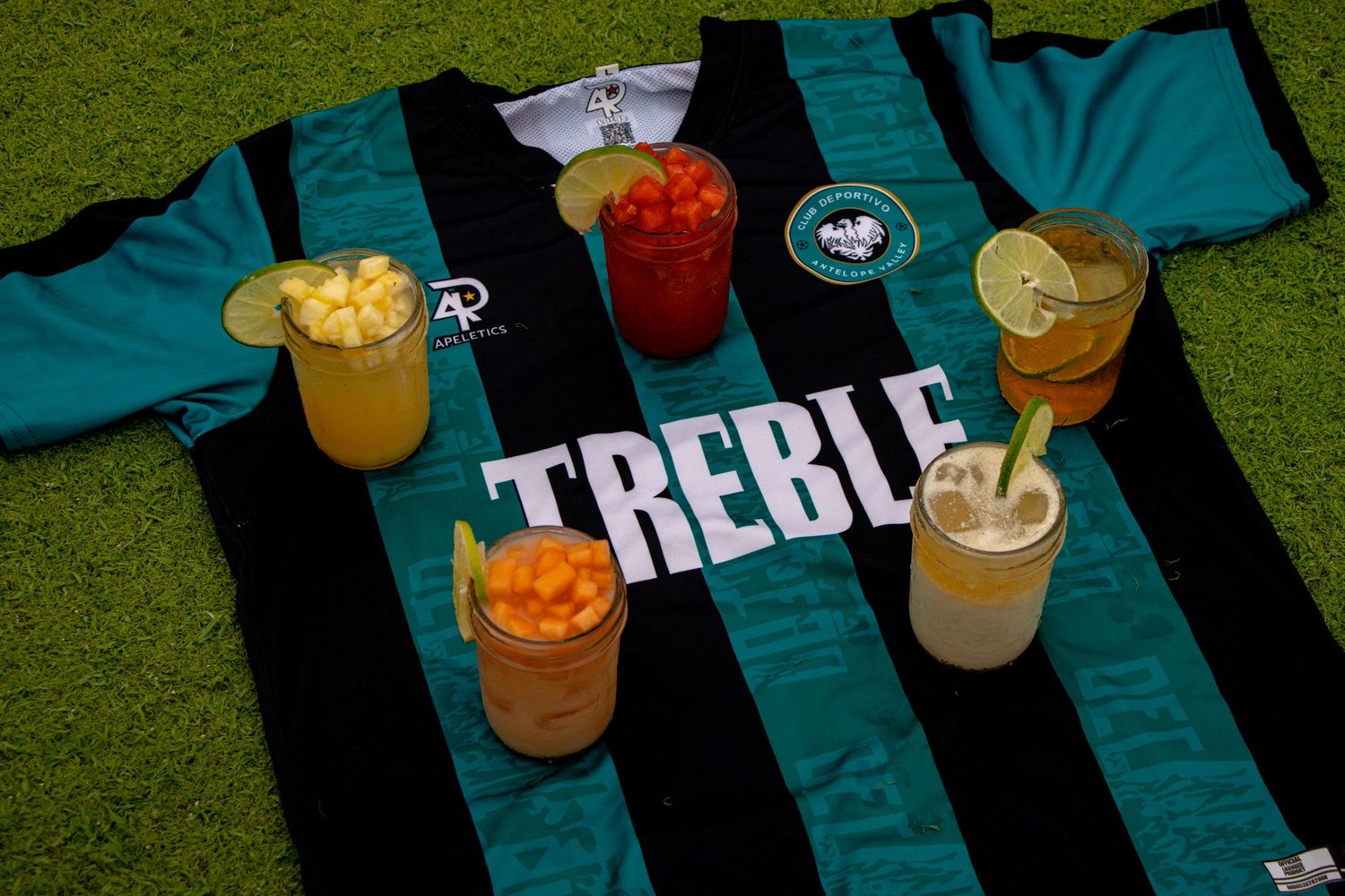 Tropical cocktails with fruit garnishes displayed on grass against green striped background.