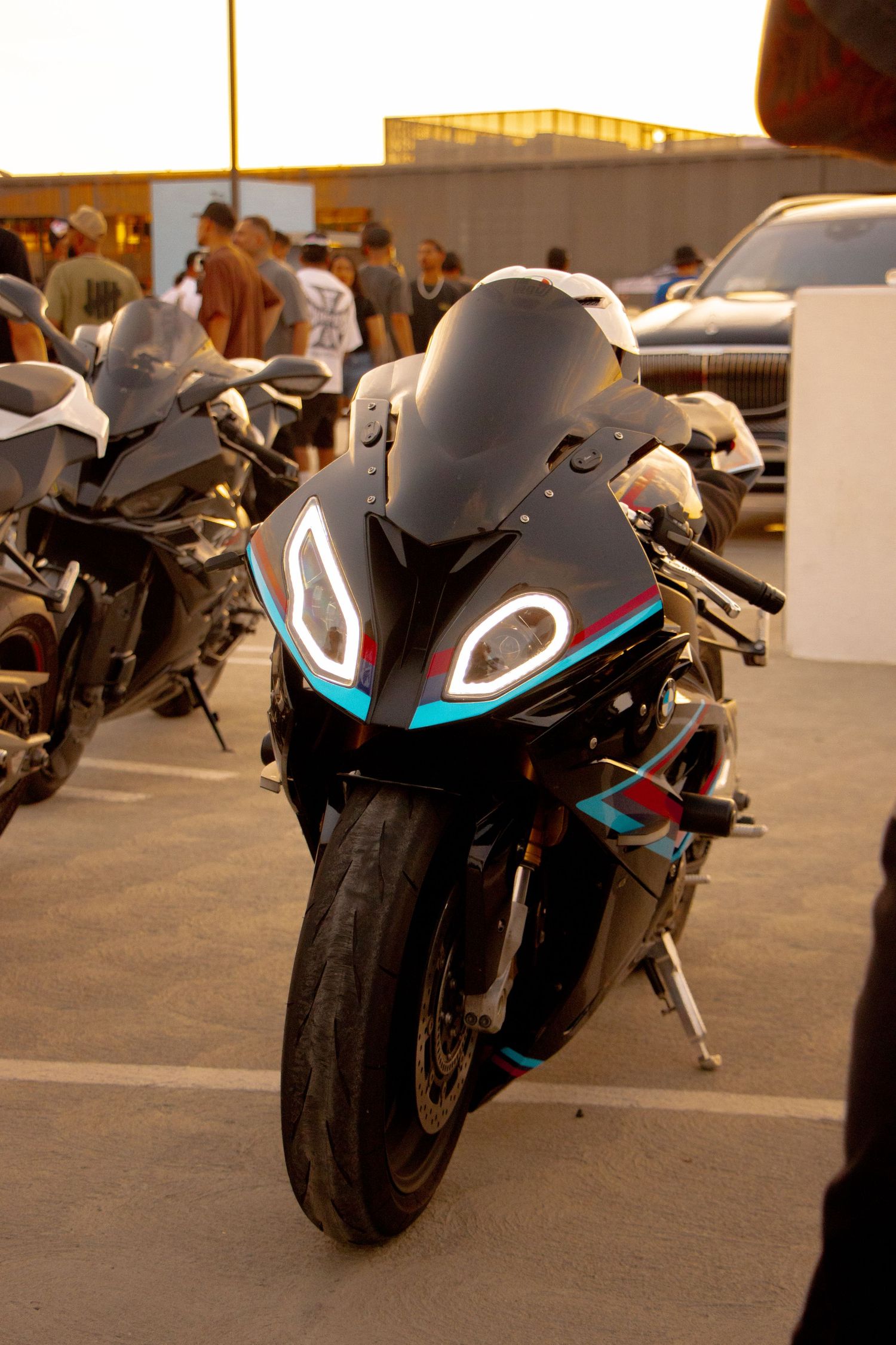 Black sport motorcycle with glowing blue and white LED headlights parked at an outdoor motorcycle meetup event.