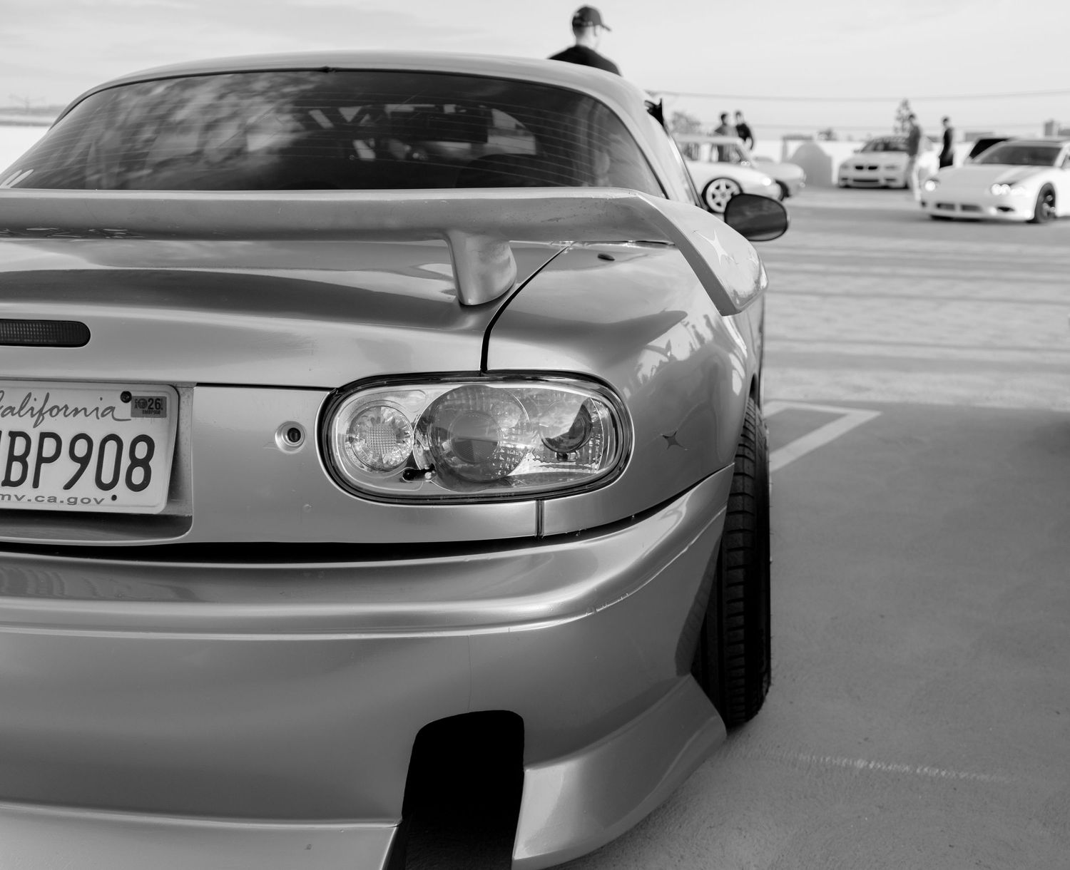 Black and white photo of a modified Toyota Supra rear end with California license plate BP908 at a car meet.
