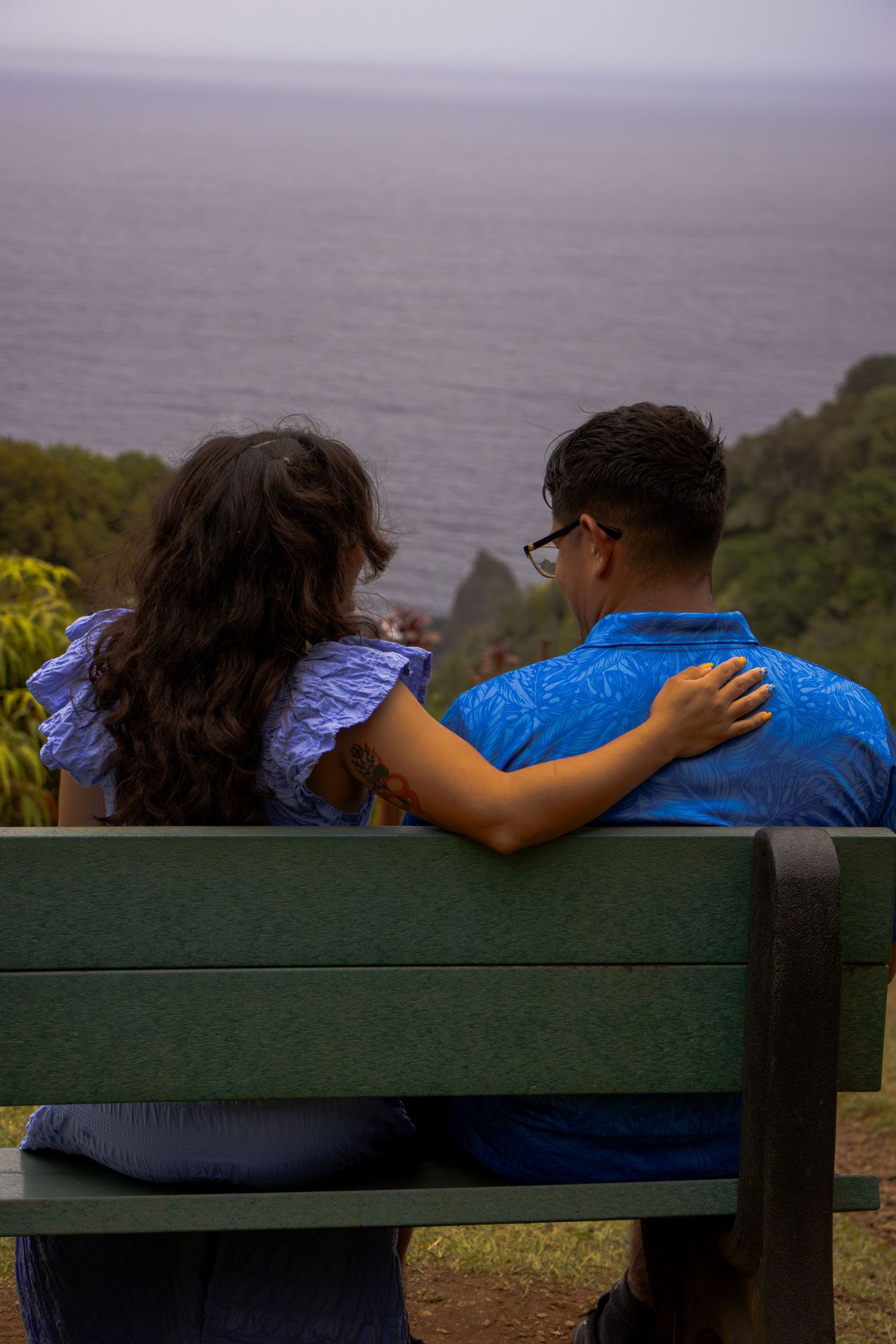 Couple sitting on bench overlooking foggy ocean view.