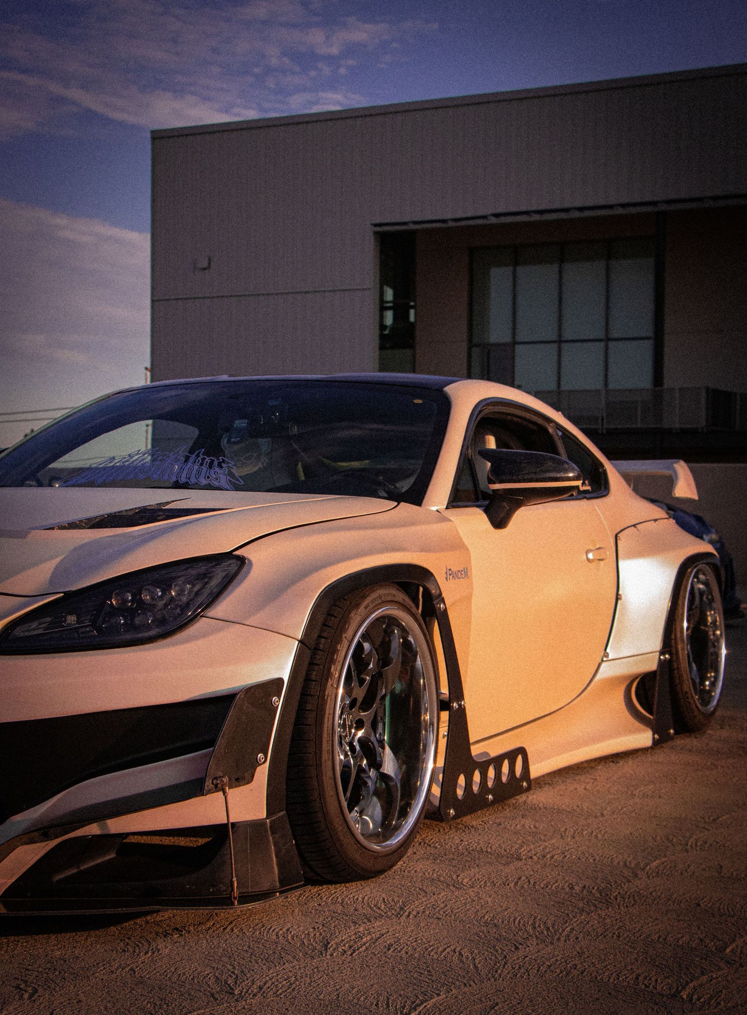 Widebody modified sports car with aggressive stance, deep dish wheels, and custom body kit parked at dusk.