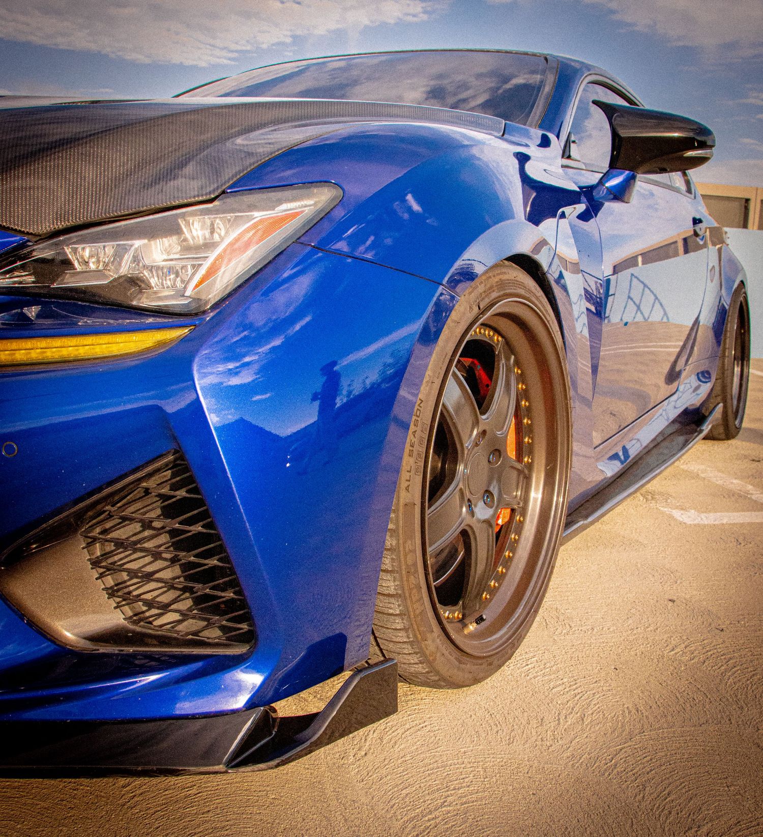 Blue Lexus RC F with bronze aftermarket wheels and red brake calipers, lowered stance on sandy surface.