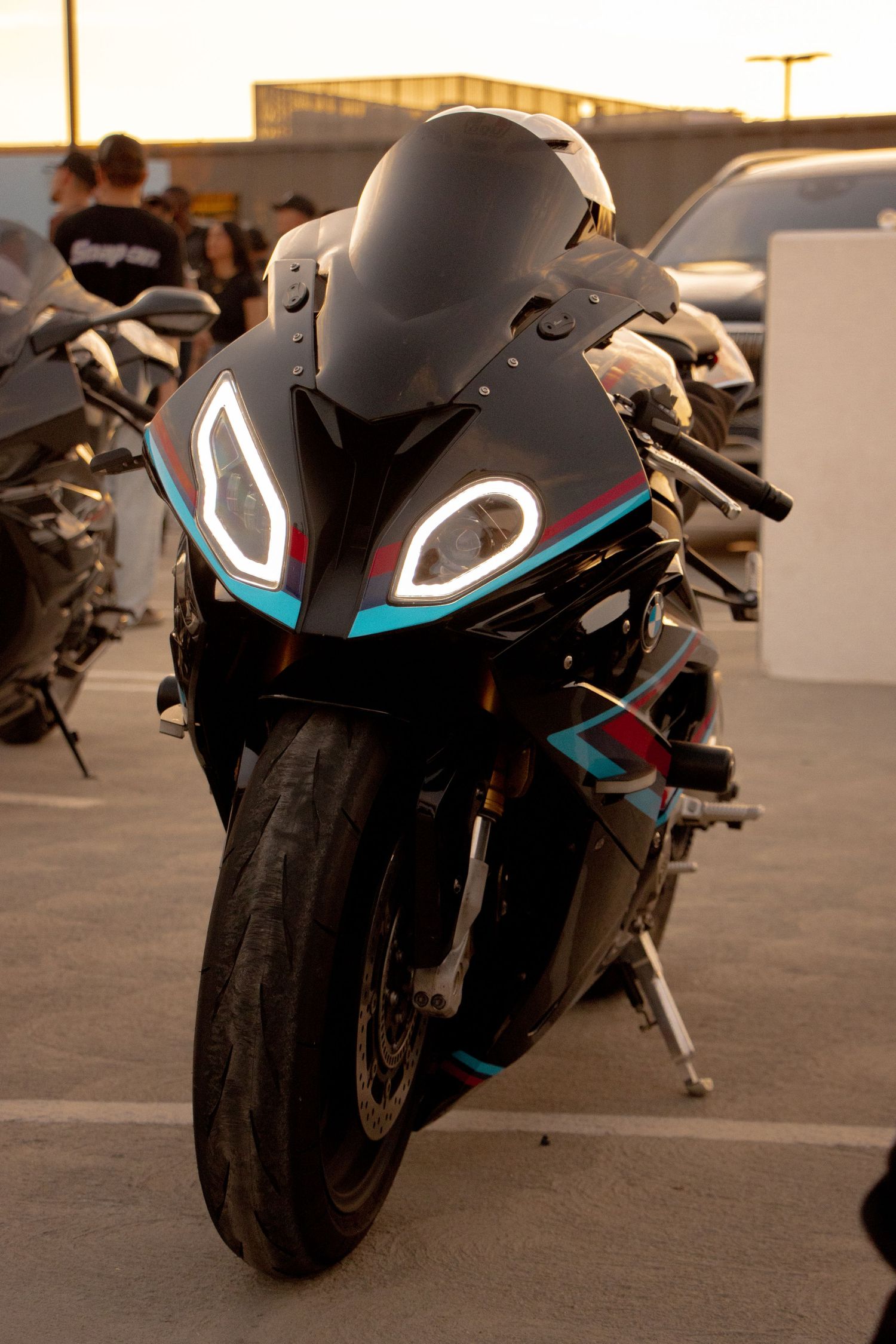 A sleek black sport motorcycle with glowing LED headlights and teal accents parked in a lot at sunset.