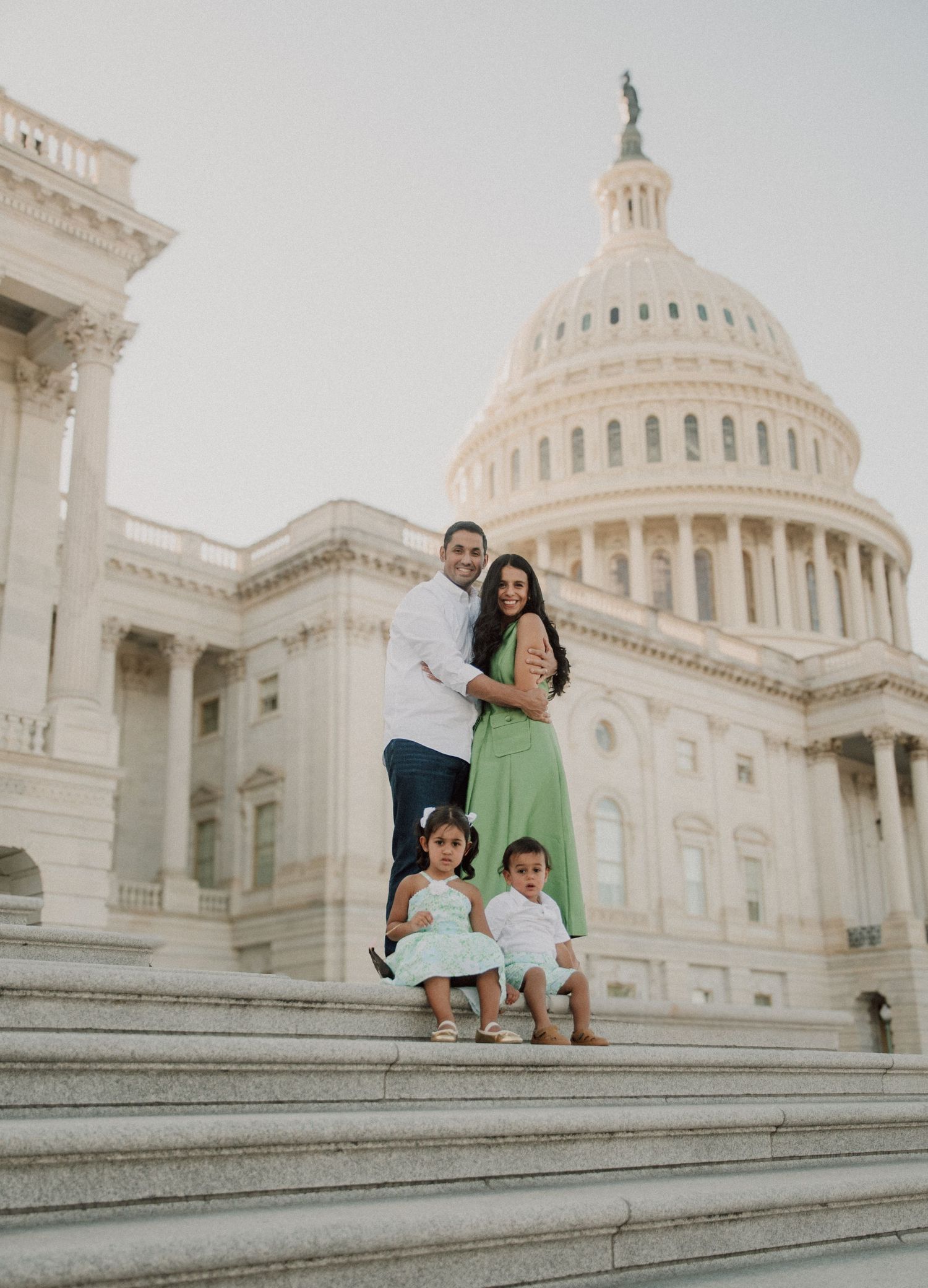 Family of four posing on the steps of the US Capitol building in Washington DC, parents and two young children smiling.