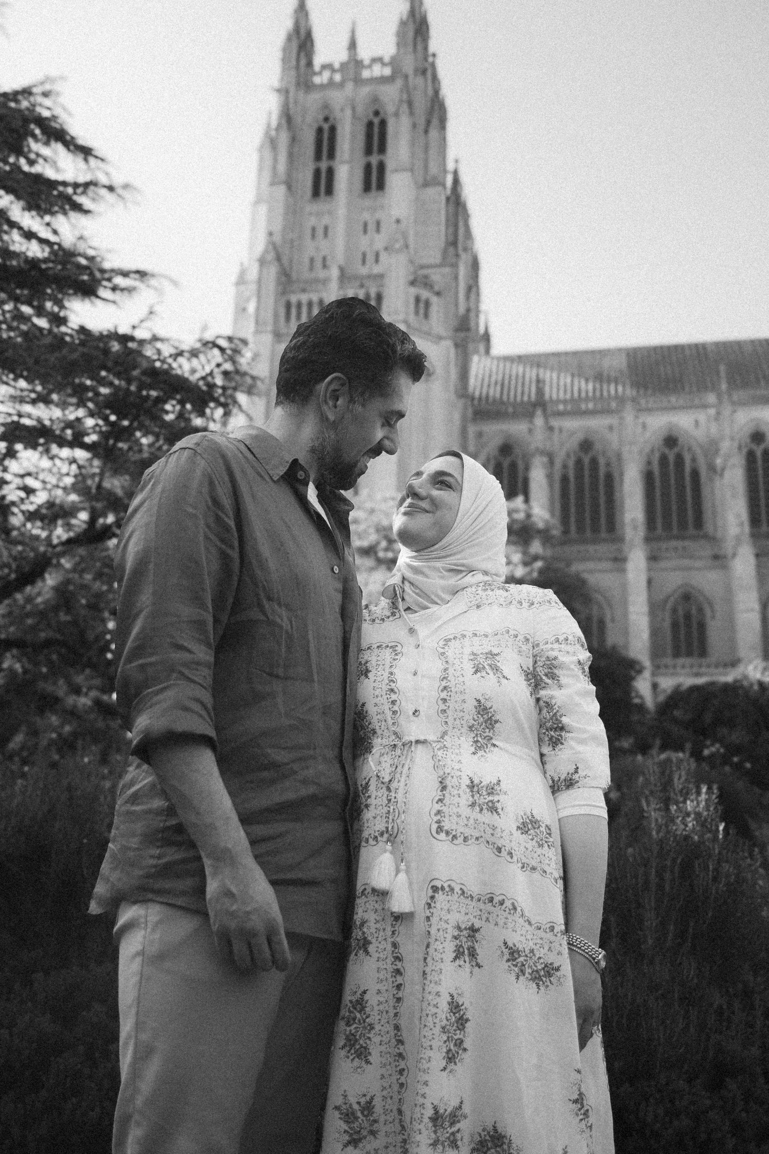 Black and white photo of a couple sharing a romantic moment in front of a grand Gothic cathedral.