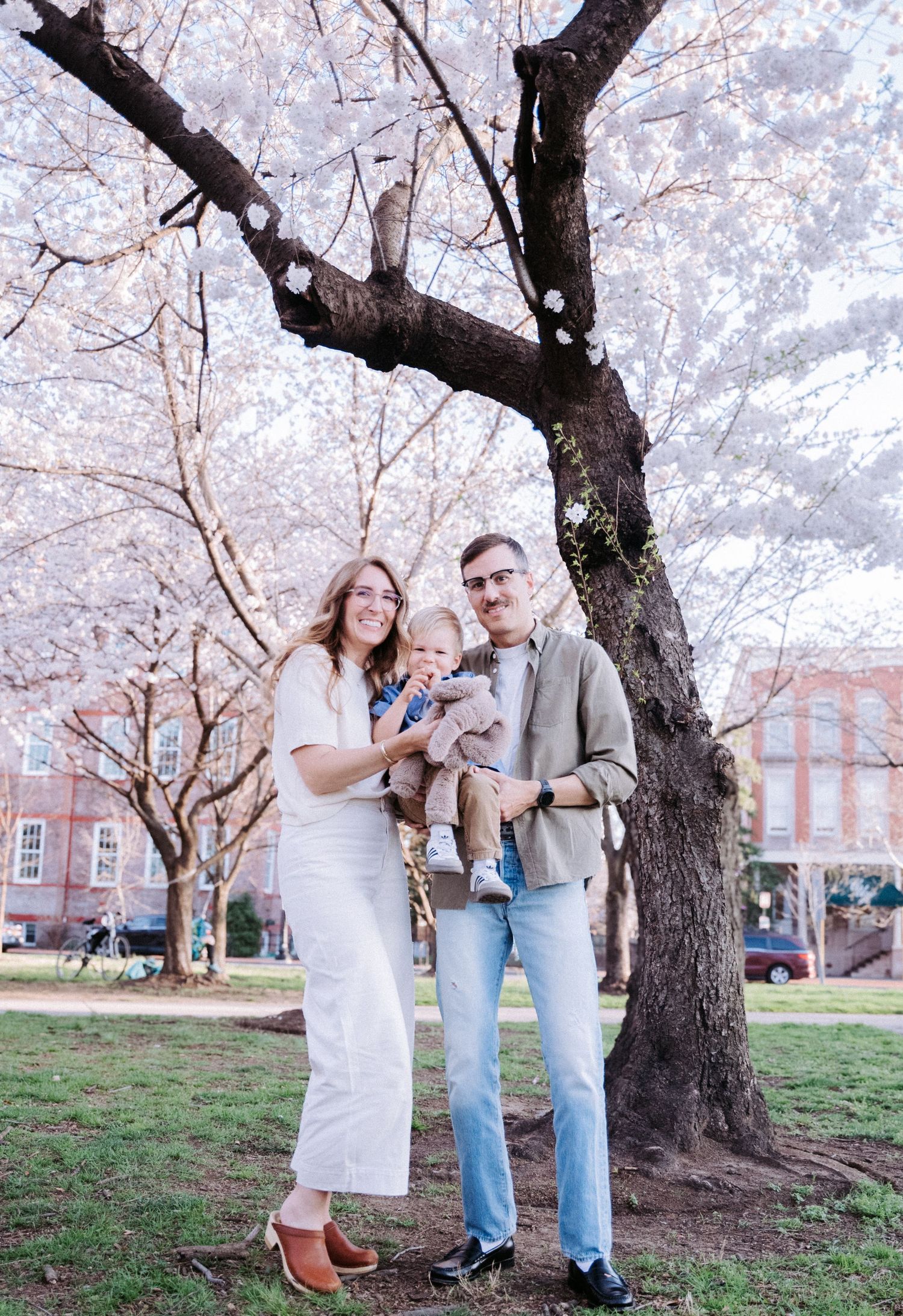 Family gathering under blooming cherry trees with white petals creating a magical spring atmosphere.
