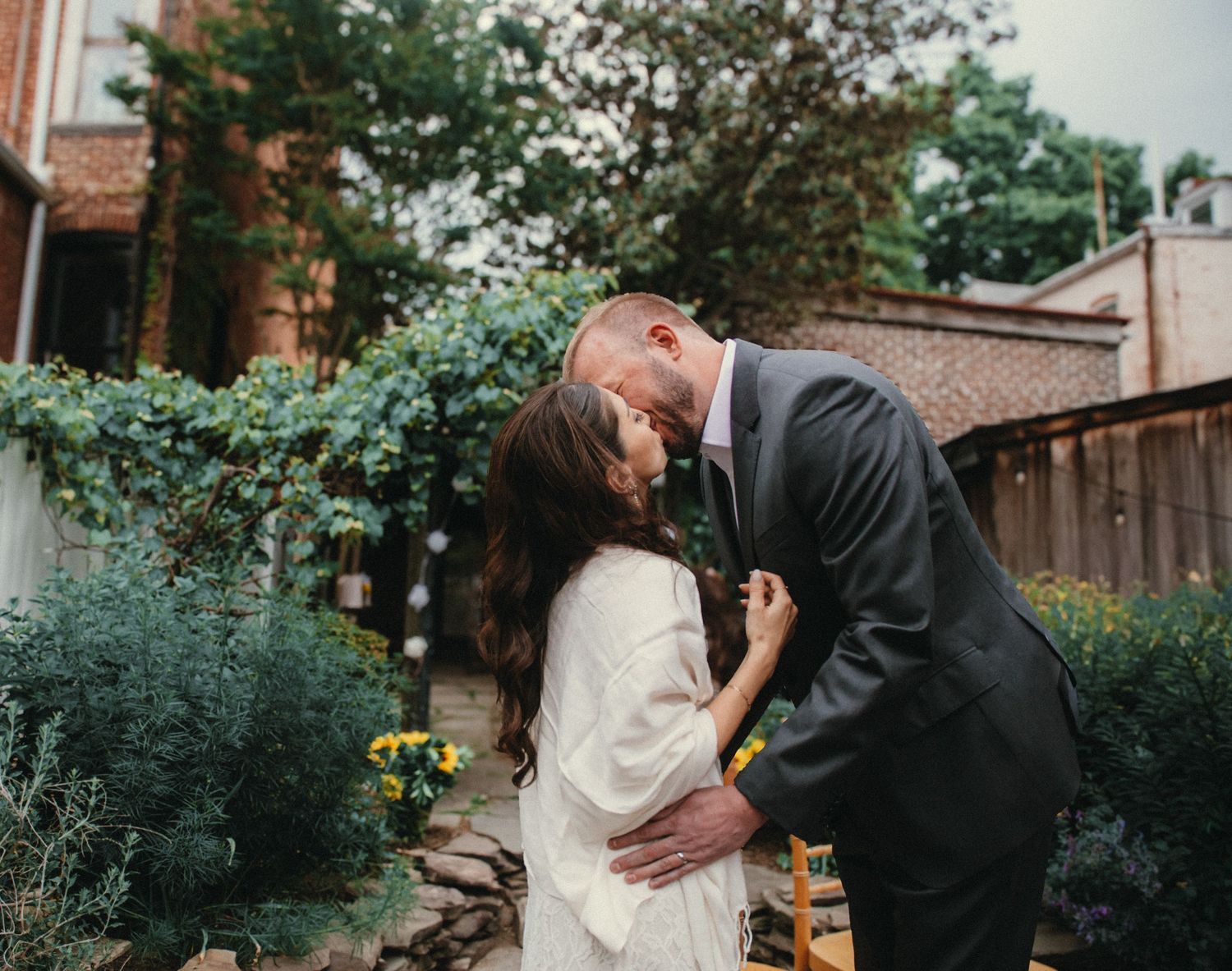 Couple sharing a romantic kiss in a lush garden during their outdoor wedding ceremony.