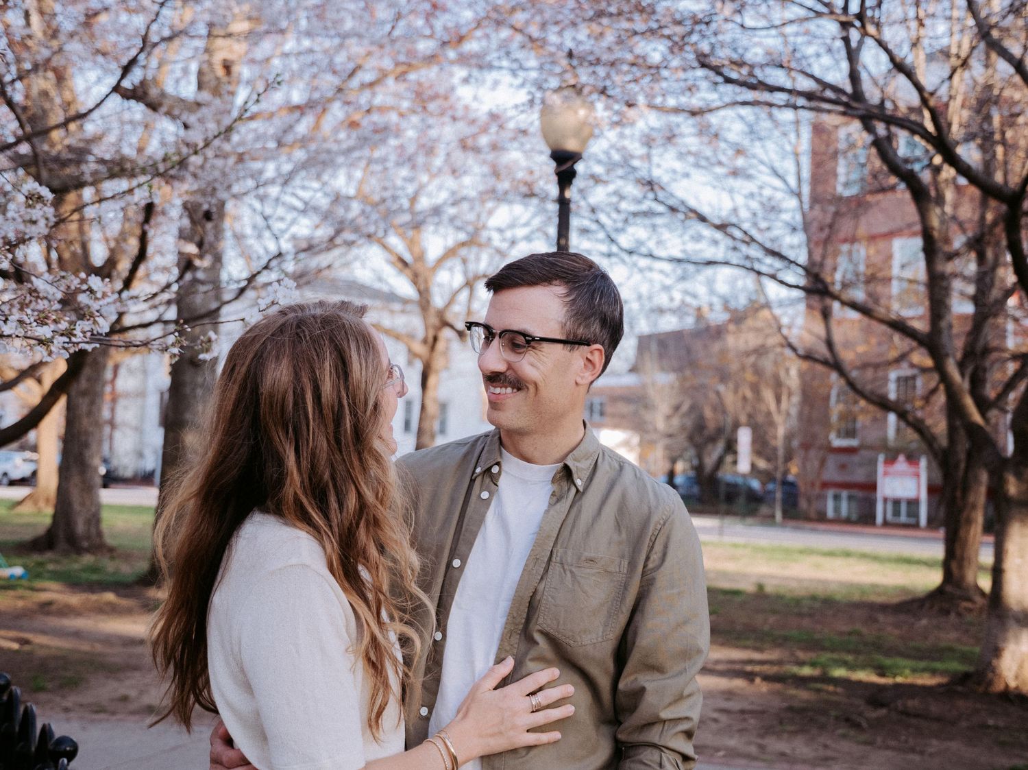 A springtime photoshoot under cherry blossom trees with brick buildings in background.