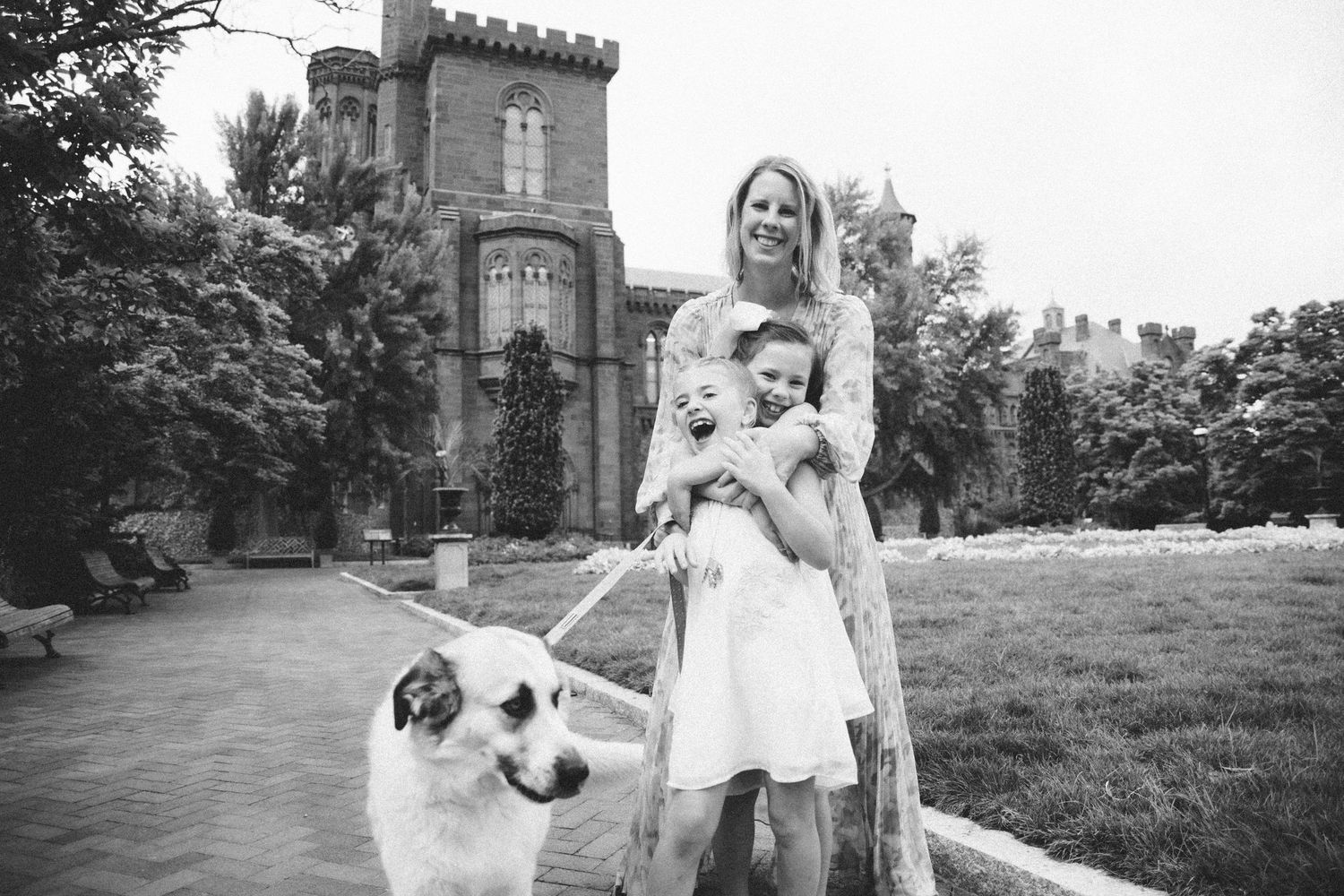 Black and white photo of a woman with a child and a dog in front of a historic castle building.