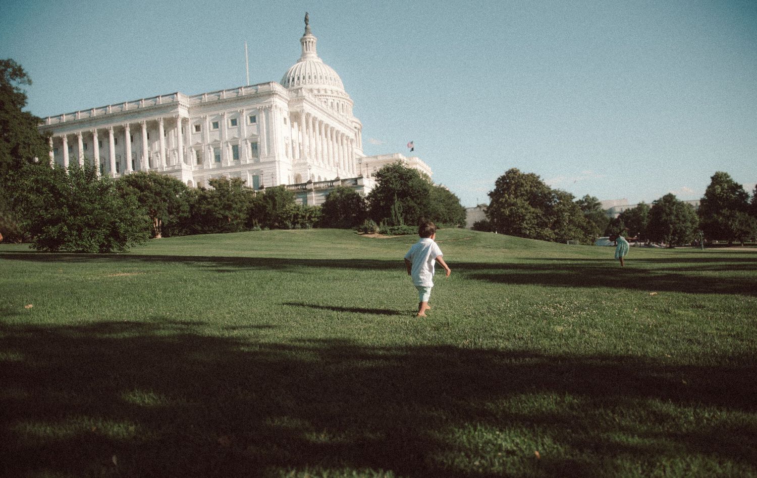 Child running on green lawn near the U.S. Capitol building in Washington D.C. on a sunny day.