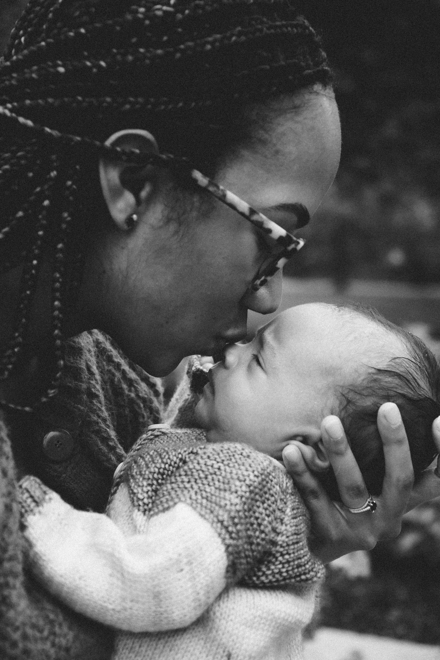 Black and white photo of a mother tenderly kissing her newborn baby while cradling the infant in her arms.