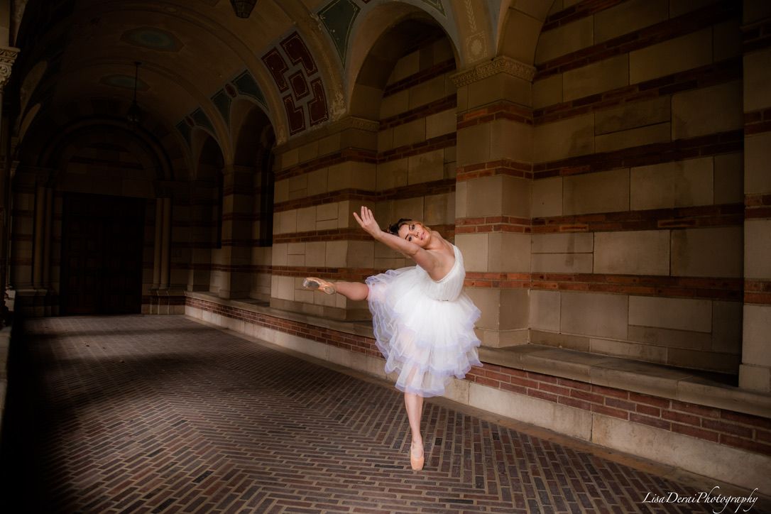 Ballerina in white tutu dances through stone corridor with arched columns.